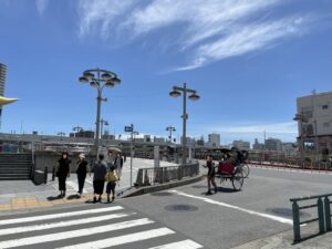 吾妻橋のたもとの交差点。観光客が歩いており、人力車が走っている風景。