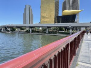 吾妻橋の赤い欄干越しに見える隅田川と、アサヒビールの金色のビルと高架道路。