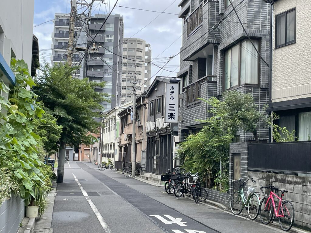 台東区日本堤二丁目の路地に建つホテル三楽と周囲の住宅や自転車が並ぶ風景