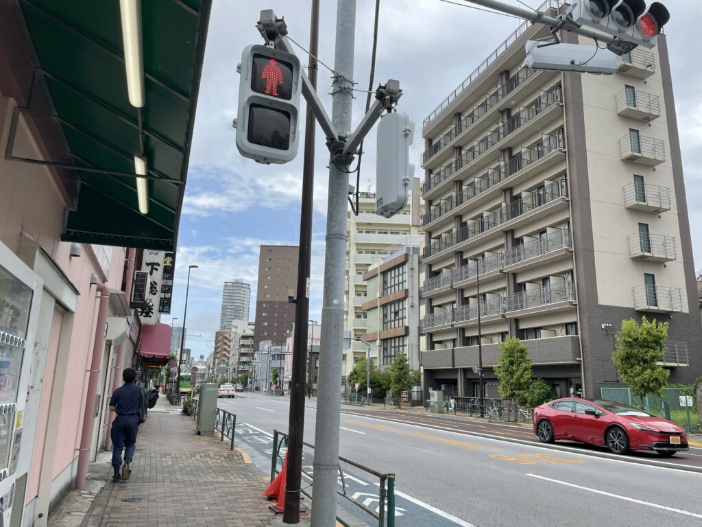 台東区日本堤二丁目の大通り沿いの歩道と信号、商店街、背後に立つ中高層マンション