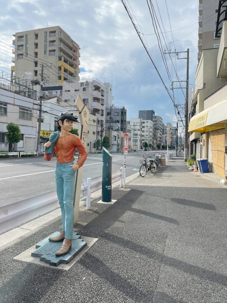 肩にジャケットをかけて立つ明日のジョーの銅像。背景には土手通りの街並み