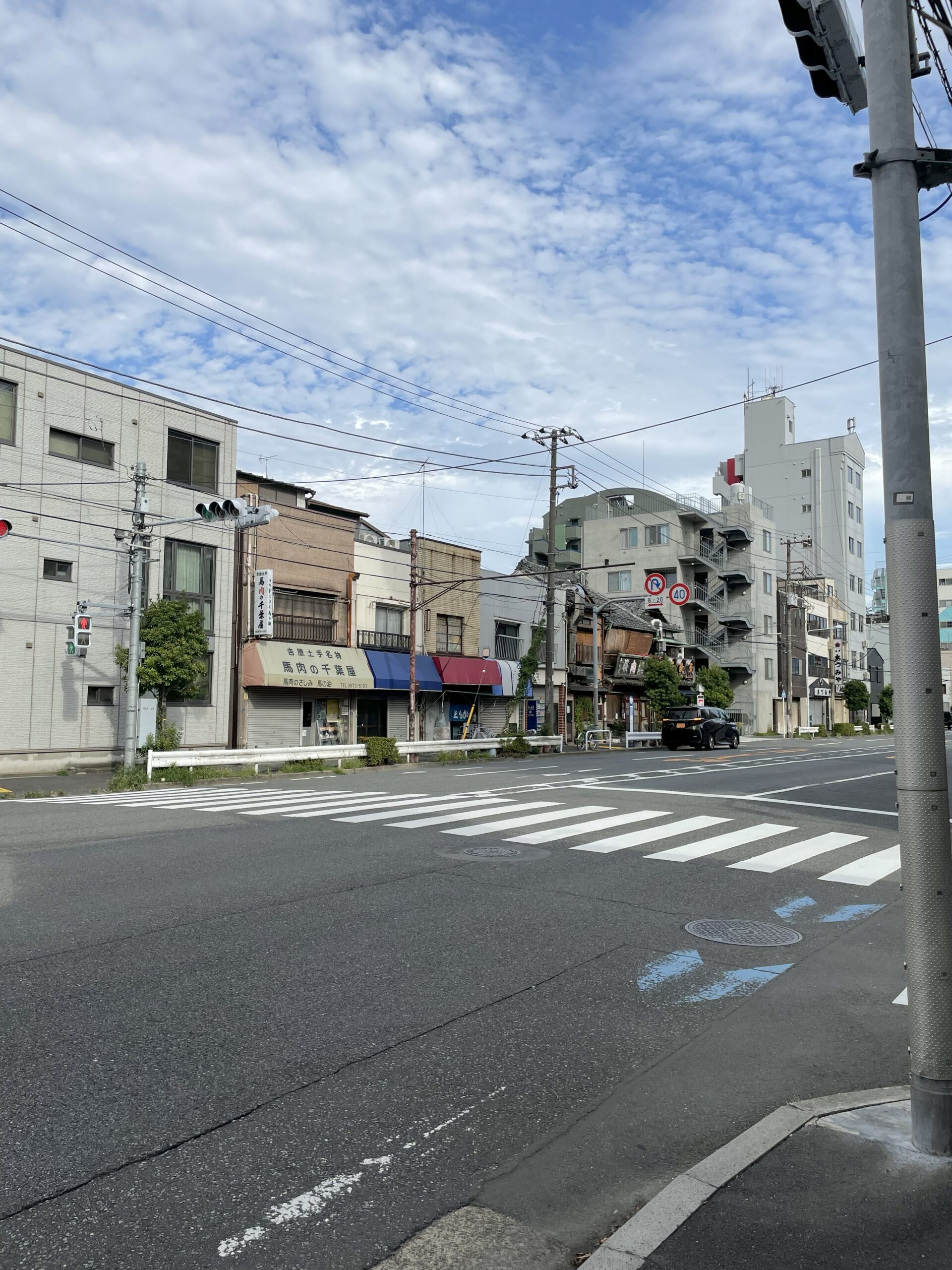 土手通りの交差点風景。青い空の下に古い商店や住宅が並んでいる