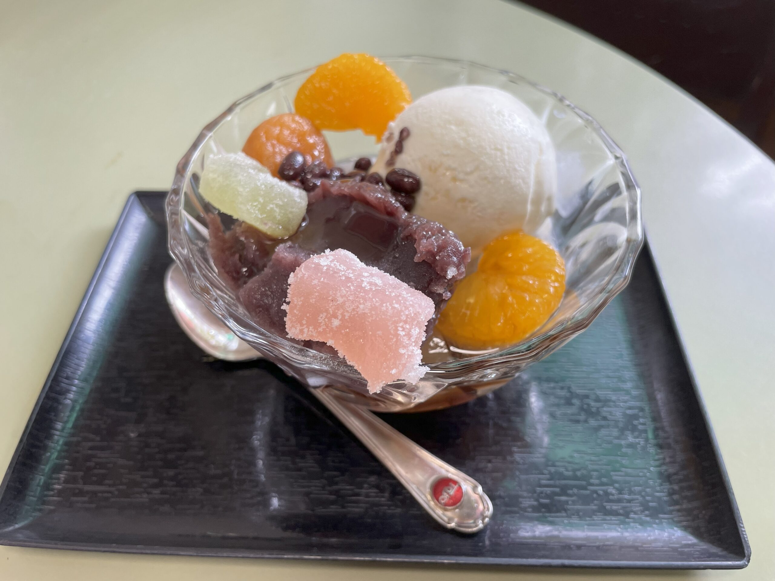 ガラスの器に盛られたクリームあんみつ。バニラアイス、小豆、みかん、求肥が彩りよく添えられている。