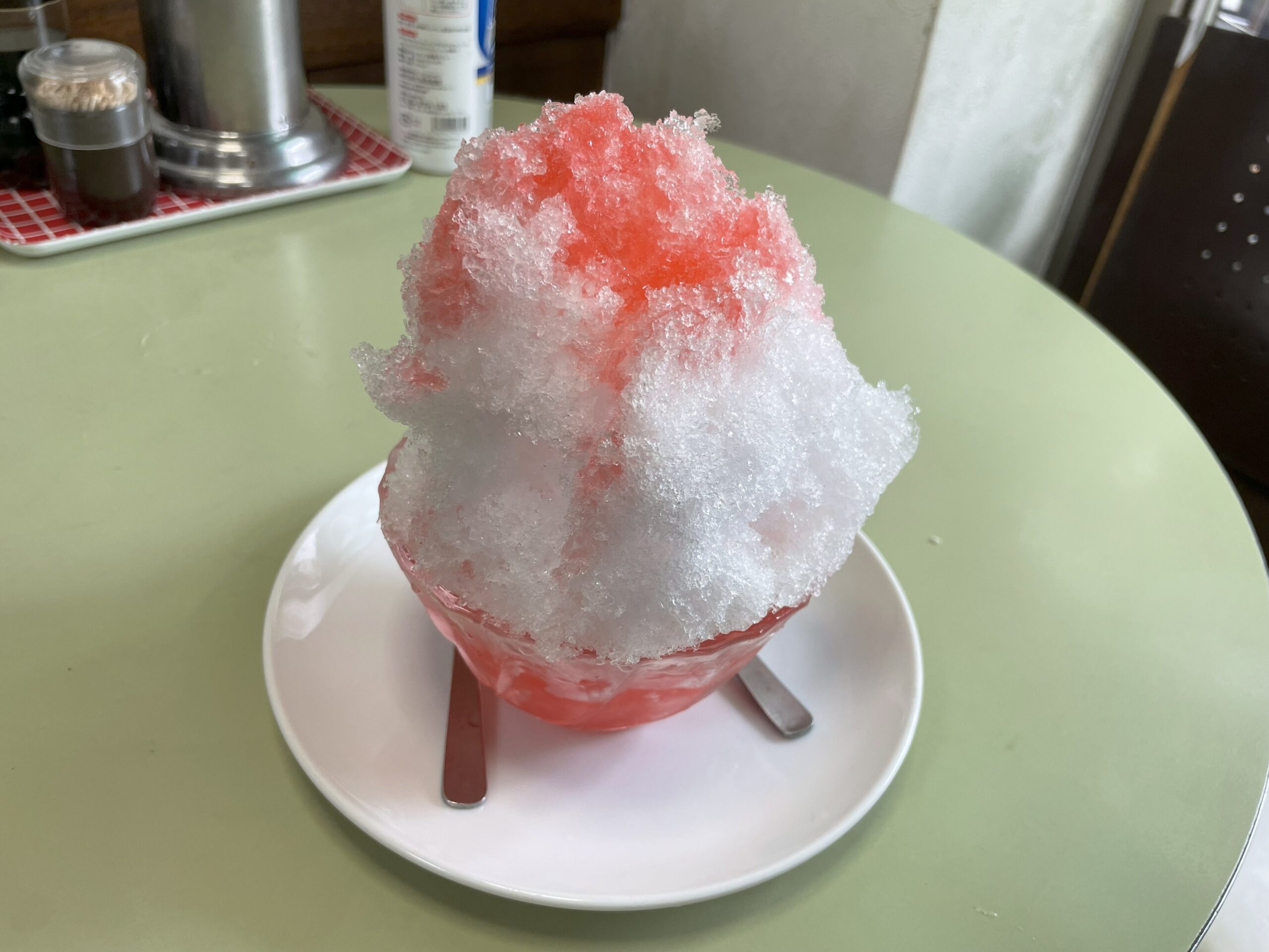 ピンク色のイチゴシロップがかかった、ふわふわのかき氷。白いお皿にのせられている。