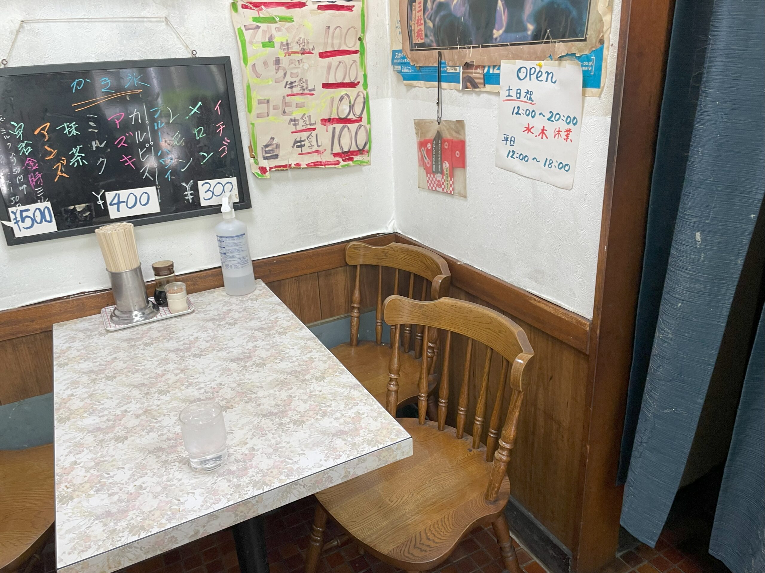 店内の小さなテーブル席。壁には手書きのかき氷メニューと営業時間の案内が掲示されている。