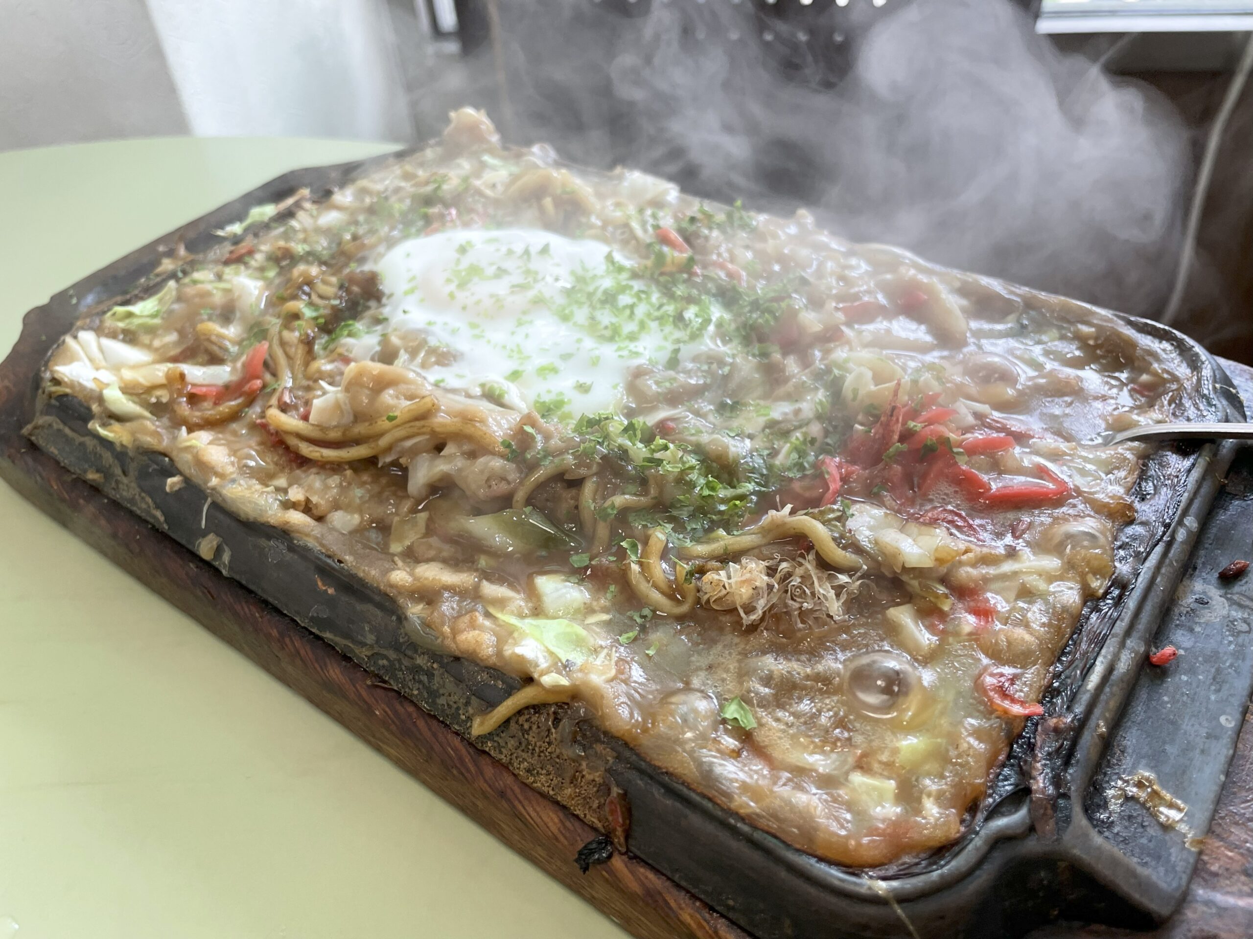 鉄板の上で熱々に仕上げられたもんじゃ焼き。中央には半熟卵がのっている。