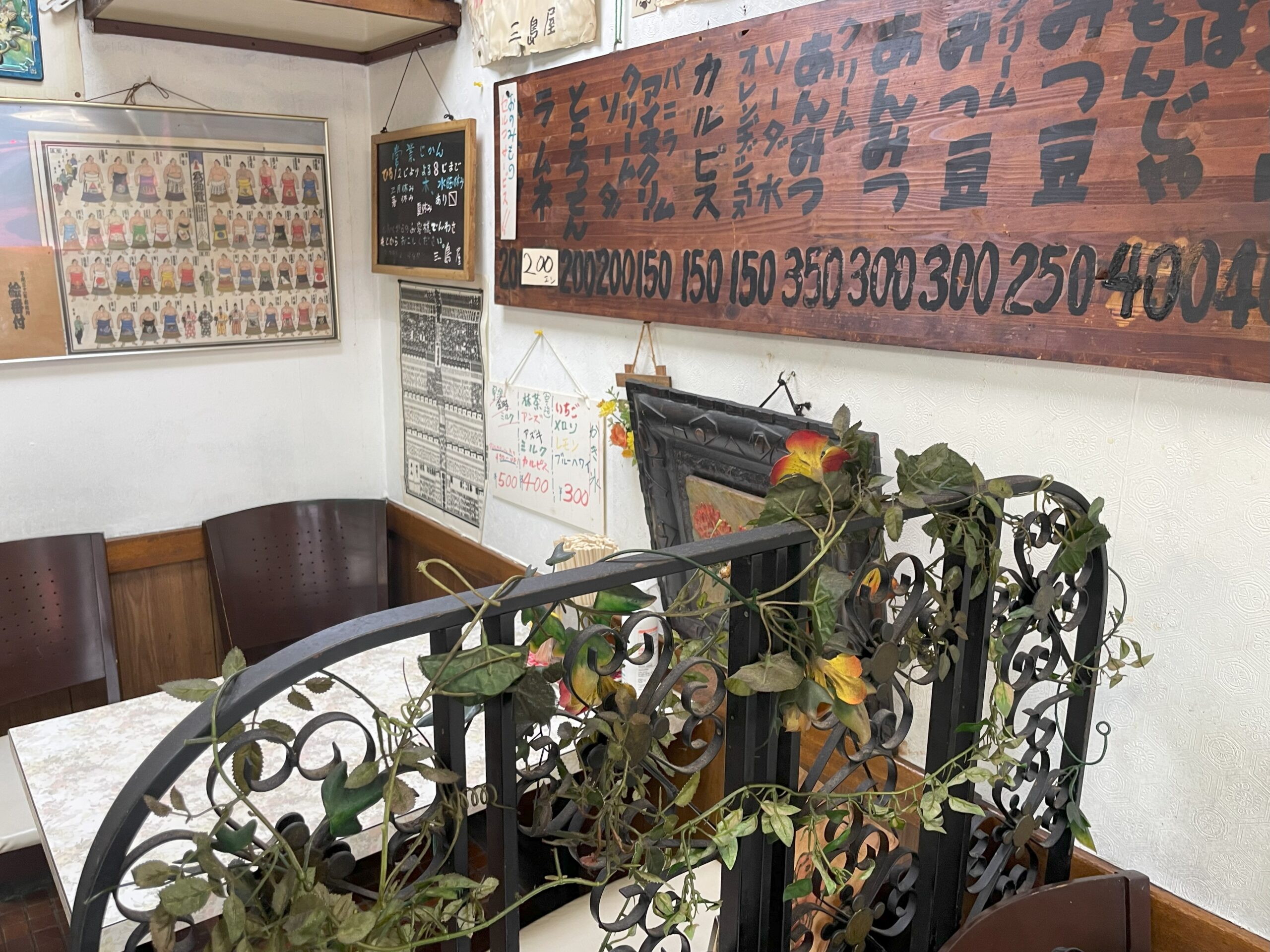 壁に木製のメニュー板が掛けられた店内。手前には観葉植物を飾った仕切りと椅子がある。