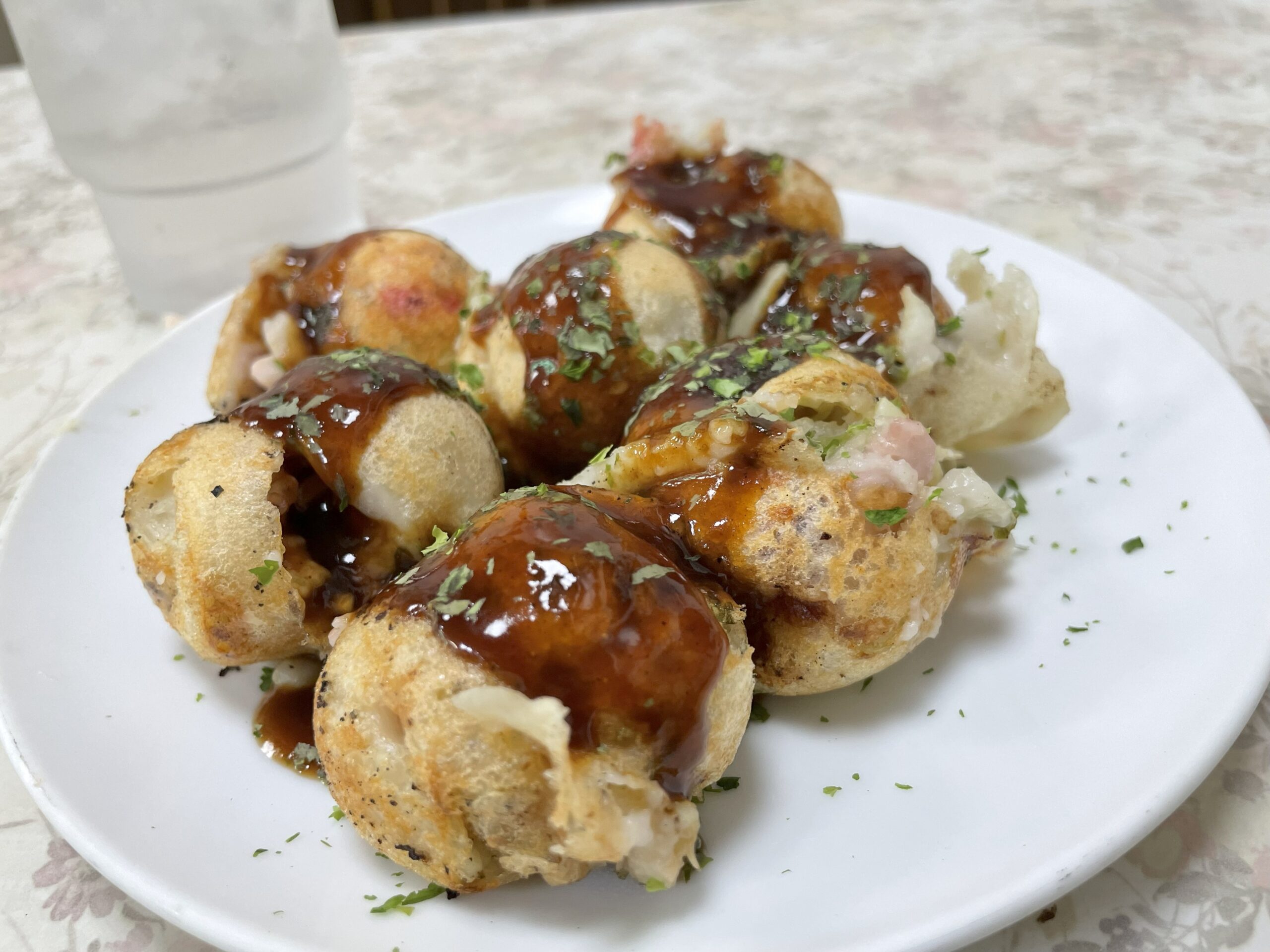 白い皿に盛られたたこ焼き。ソースがかかり、青のりがふりかけられている。