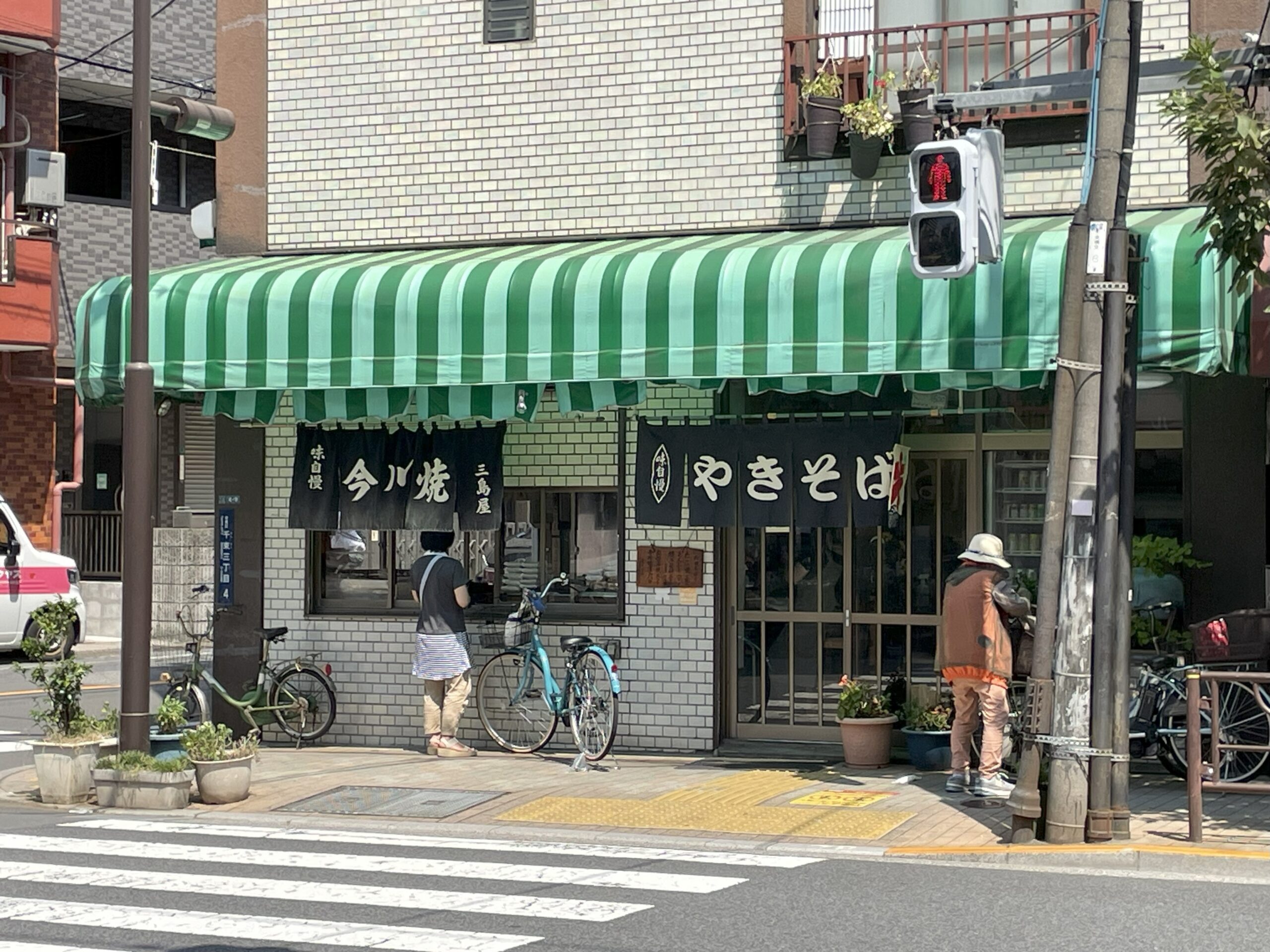 緑のテントの下に、今川焼ややきそばと書かれた暖簾。入口の横ではお客さんが注文している。