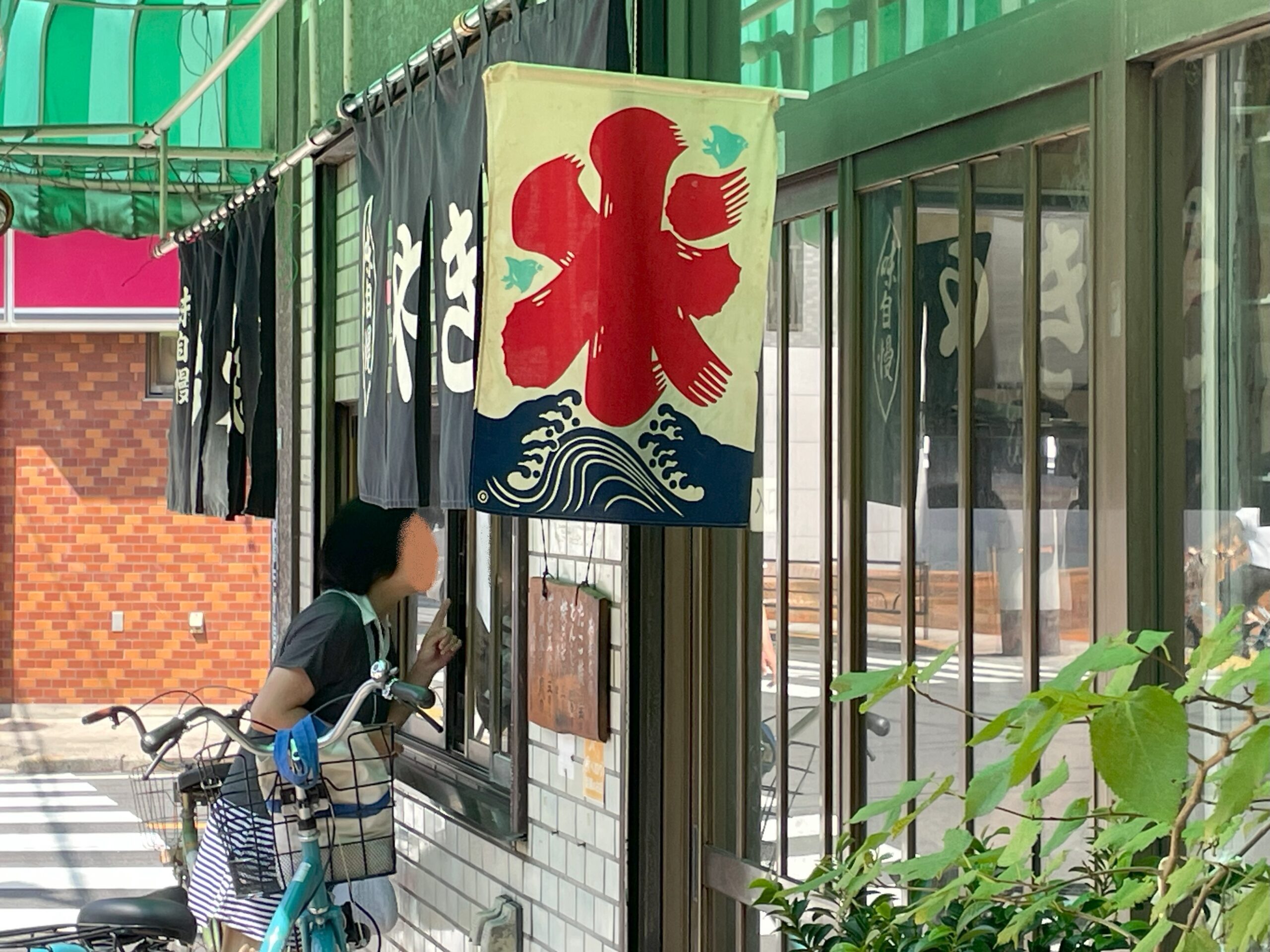 緑のテントの下、赤い「氷」の旗と黒い暖簾が掛かる店先。お客さんが窓口で注文している。