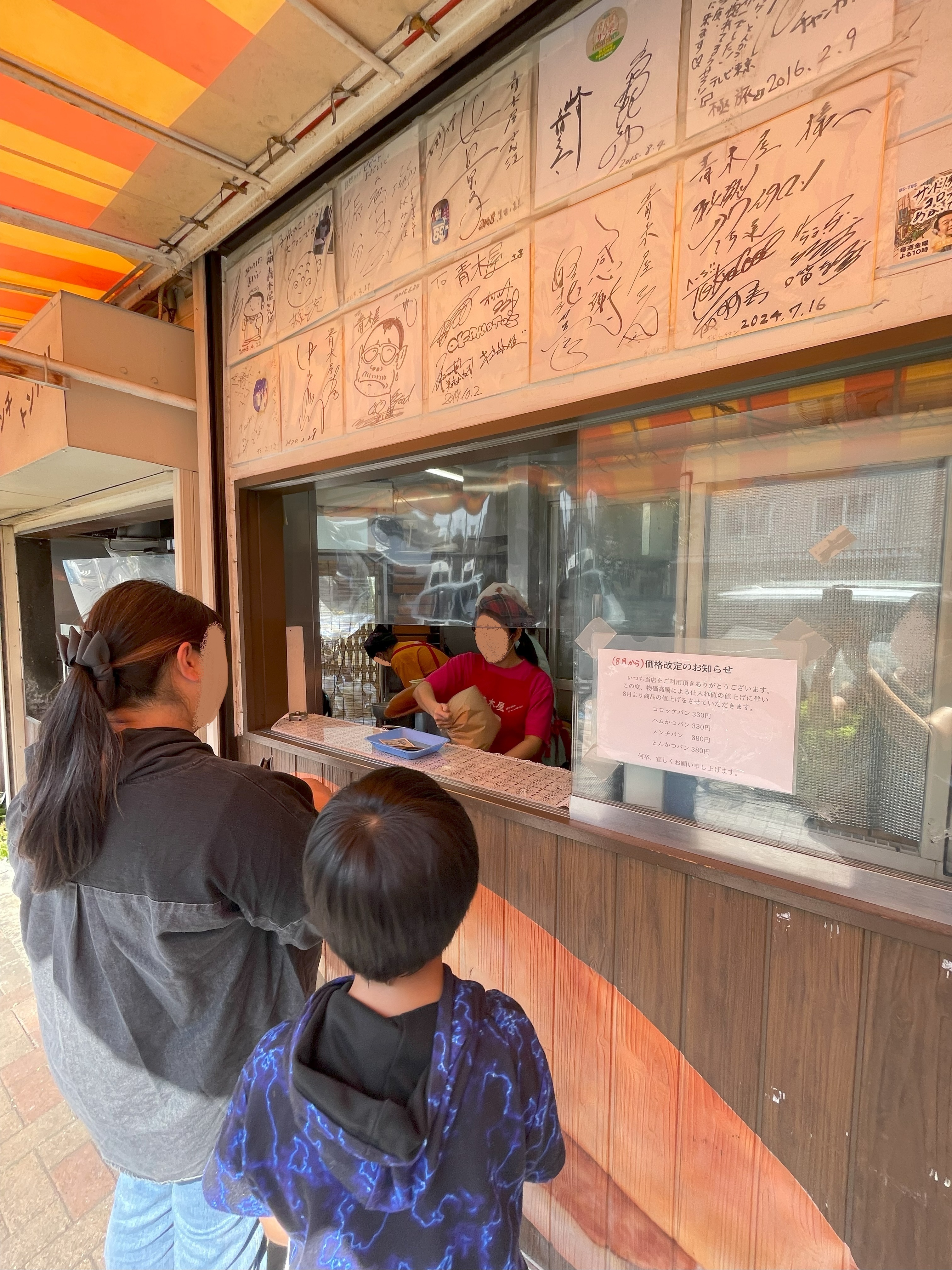 店舗のカウンターでジャンボパンを受け取る人の様子。店頭には有名人のサイン色紙が飾られている。