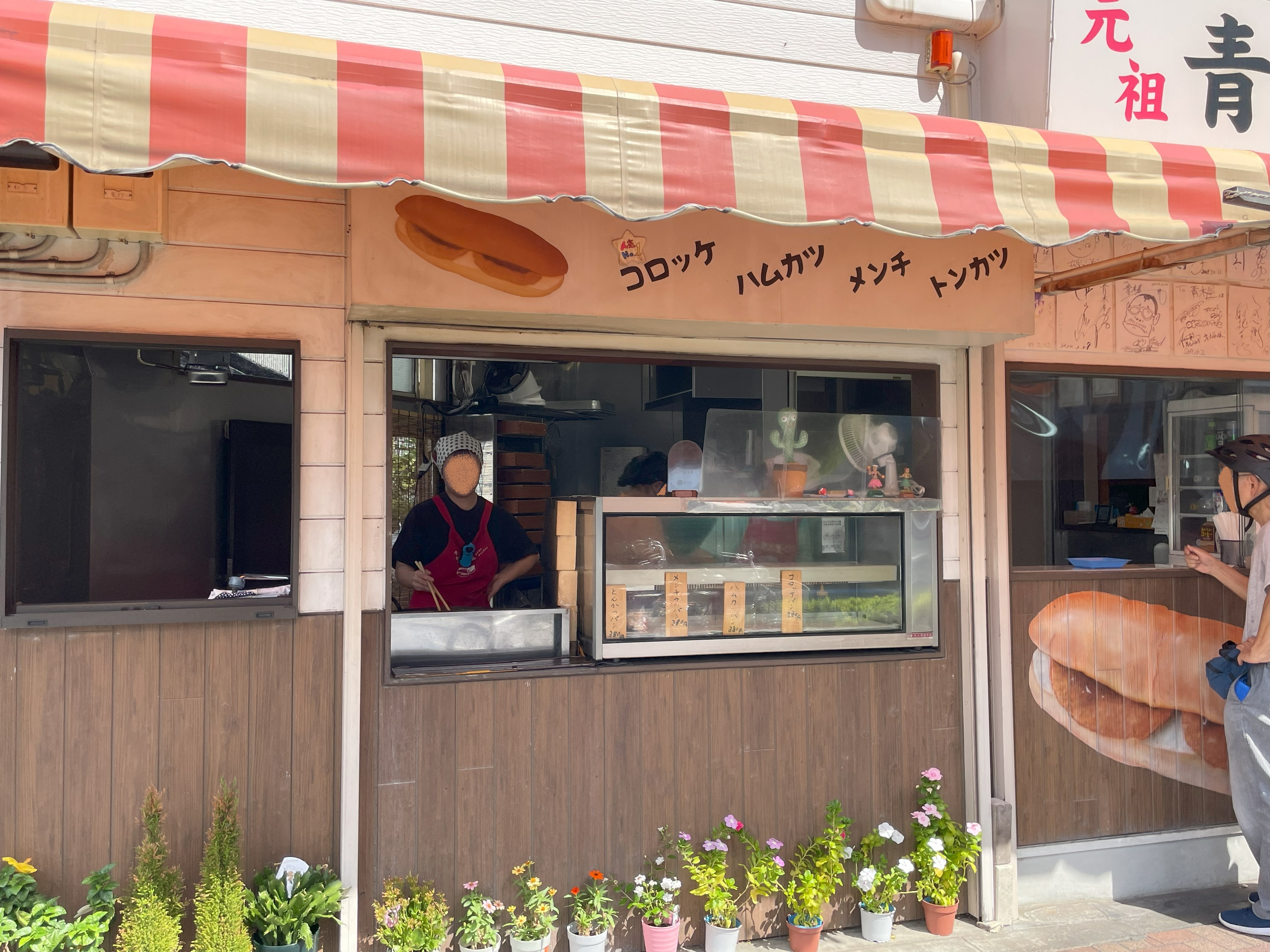 青木屋さんのカウンター内で、店員が揚げ物を調理している様子。コッペパンメニューが店頭に掲示されている。