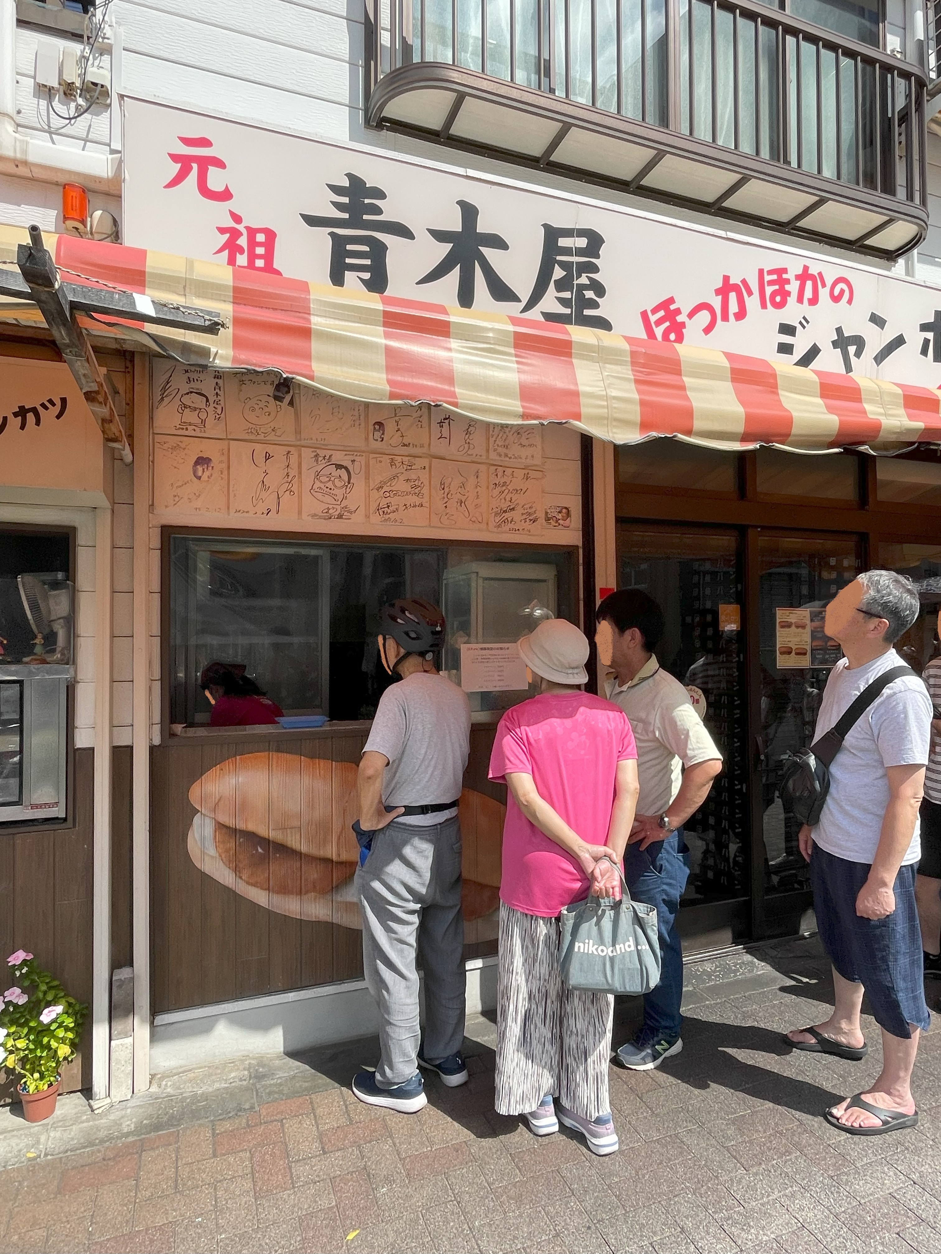 青木屋さんの店舗前でパンを待つ人々と、看板や有名人のサインが並ぶ店の外観。