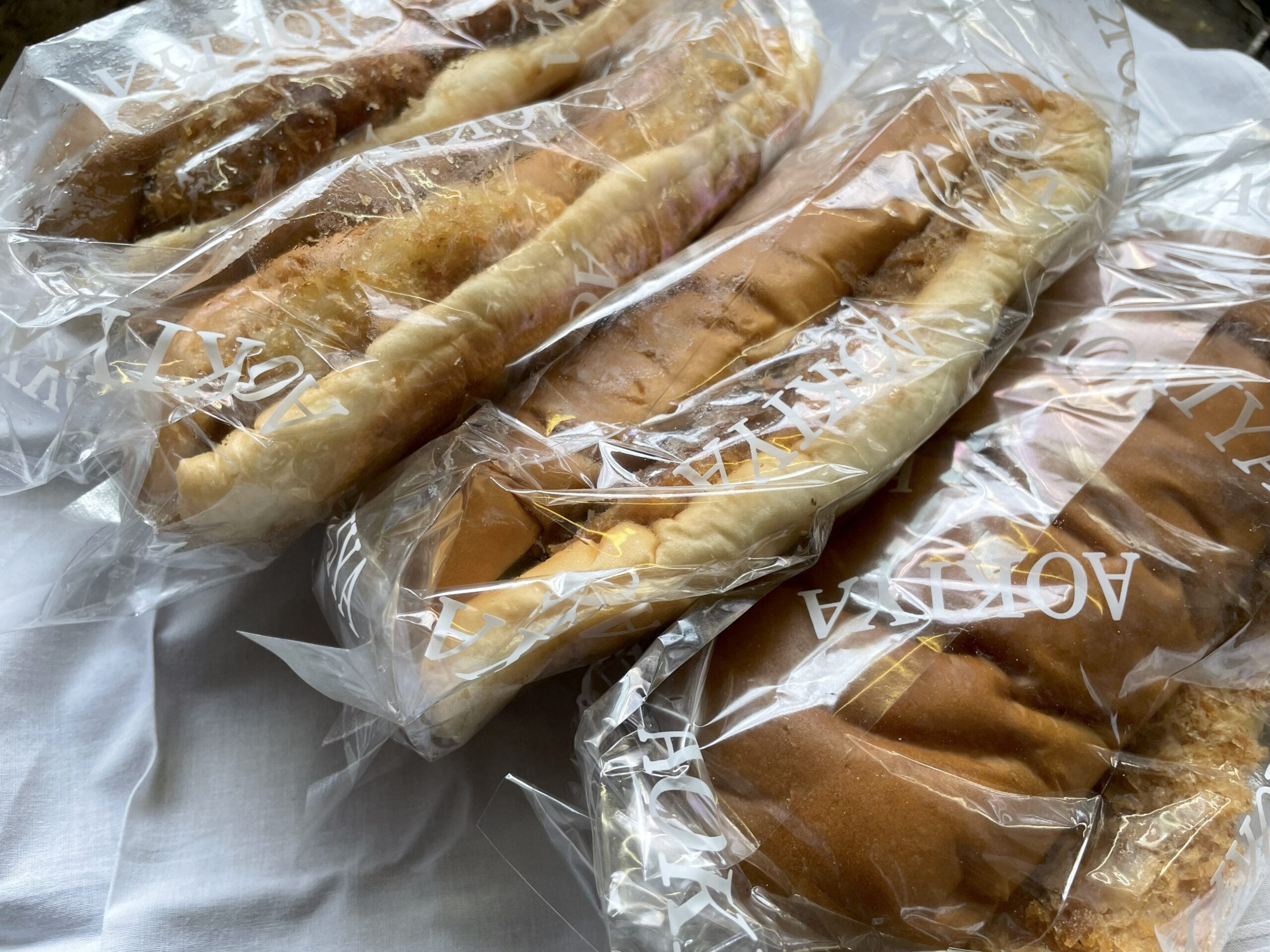 青木屋さんのコロッケパン、ハムカツパン、メンチカツパン、とんかつパンが透明な袋に入って並べられている。