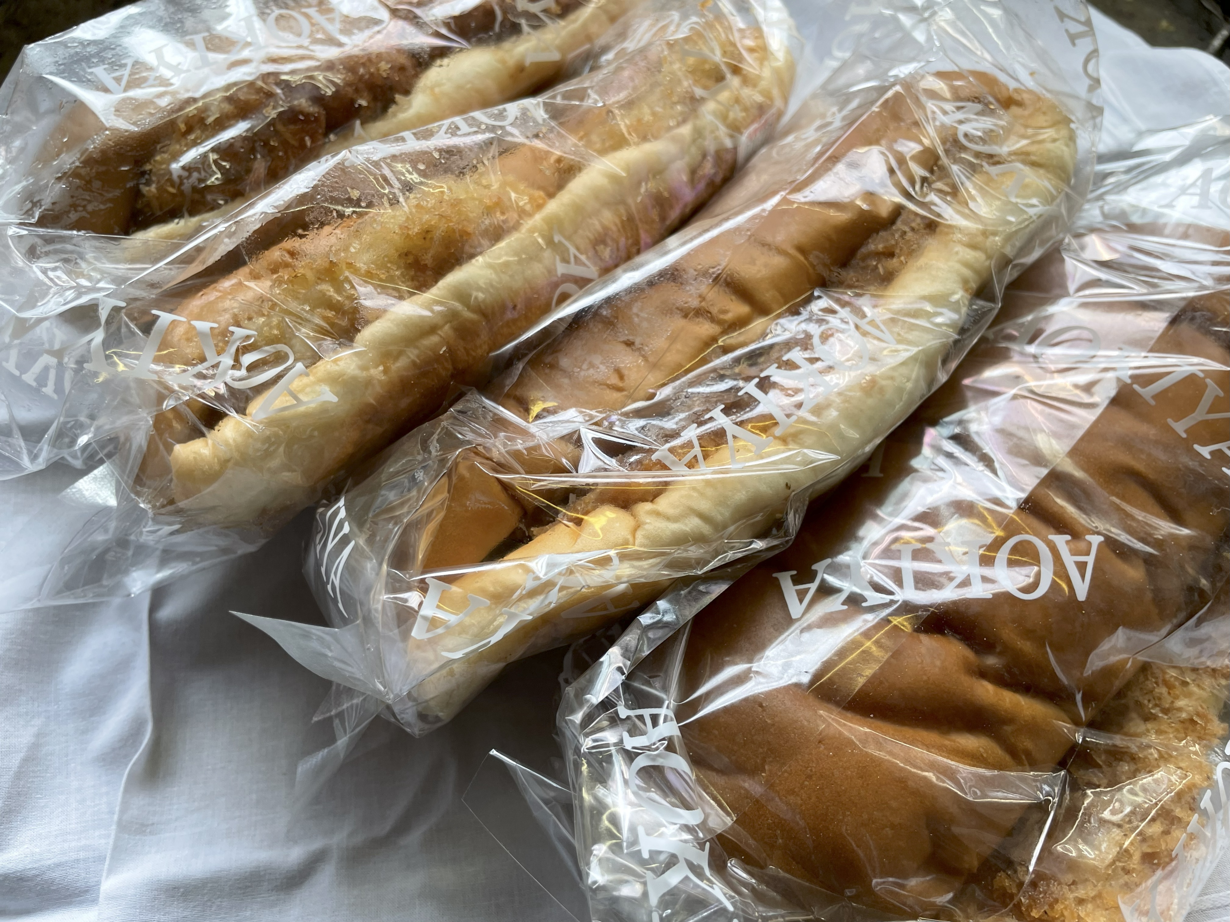 青木屋さんのコロッケパン、ハムカツパン、メンチカツパン、とんかつパンが透明な袋に入って並べられている。