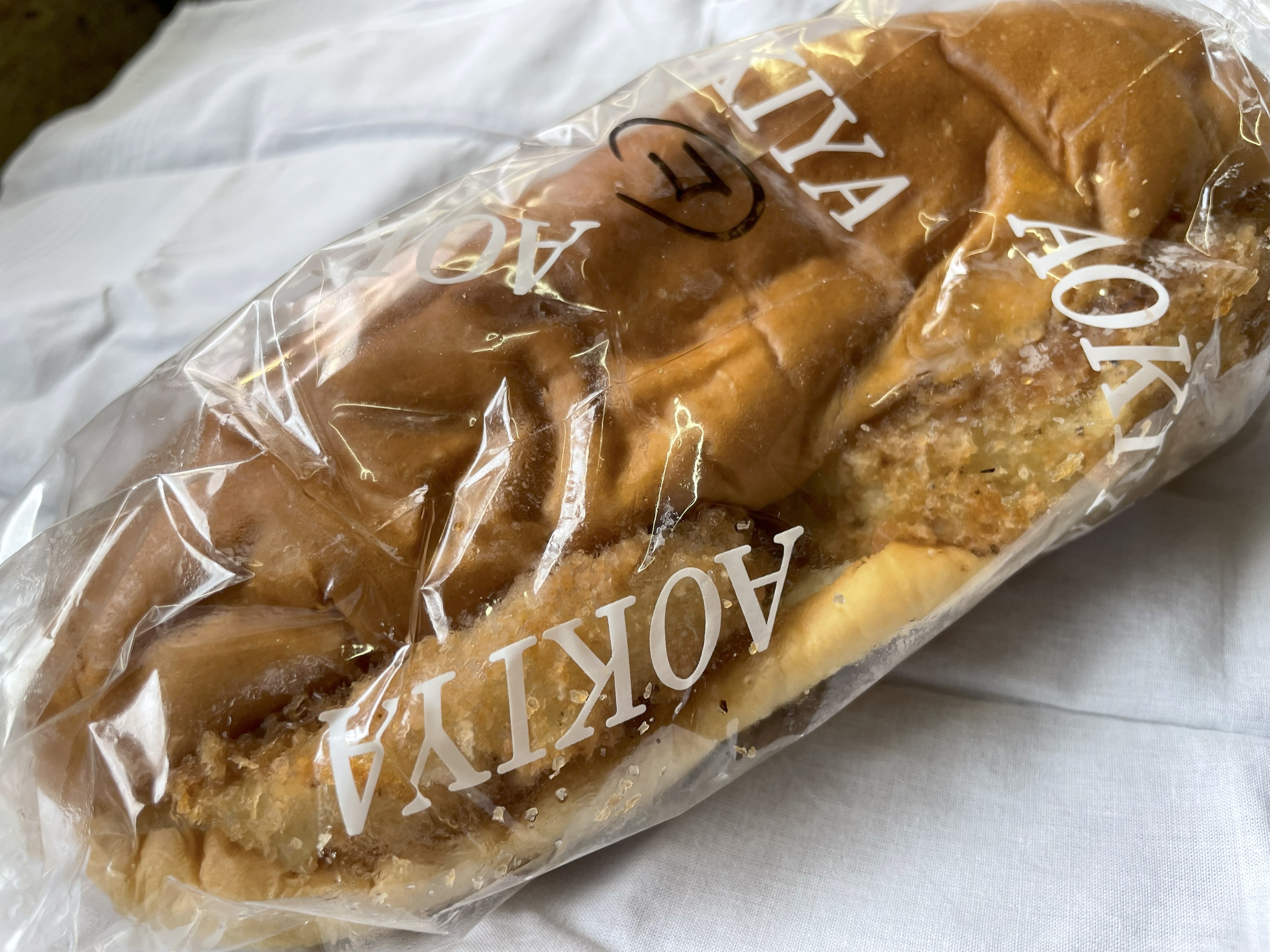 袋に包まれた青木屋さんのコロッケパン。ふんわりしたパンに大きなコロッケが挟まれている。