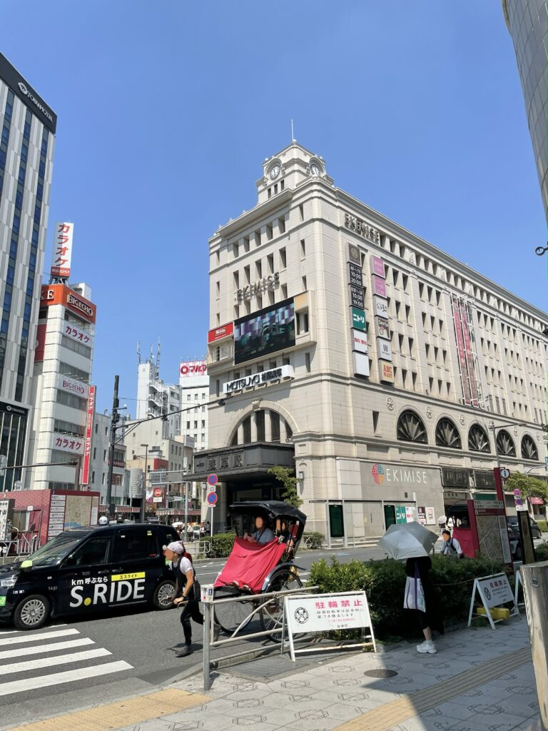 夏の青空の下。百貨店「松屋浅草」前のバス通りを、タクシーや人力車が走っている。