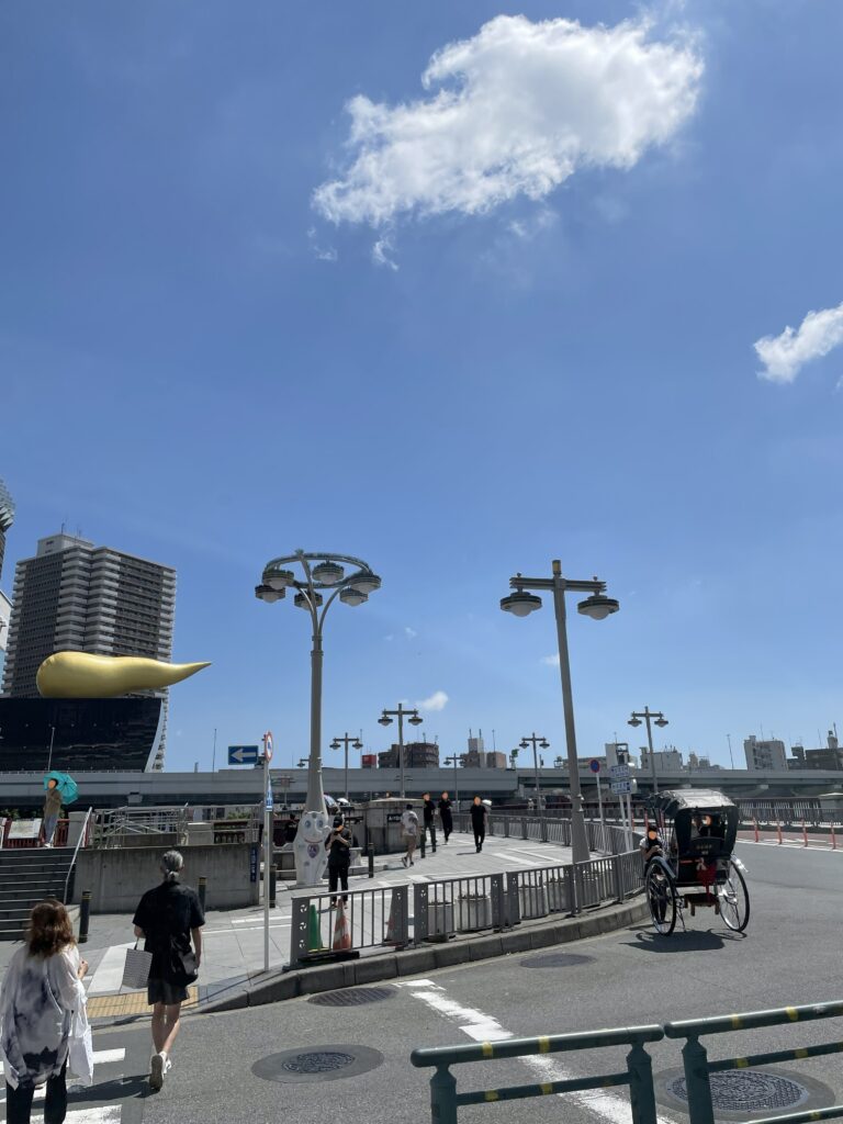 隅田川にかかる吾妻橋を、人力車や人々が行きかっている。吾妻橋を渡ると墨田区に入る。