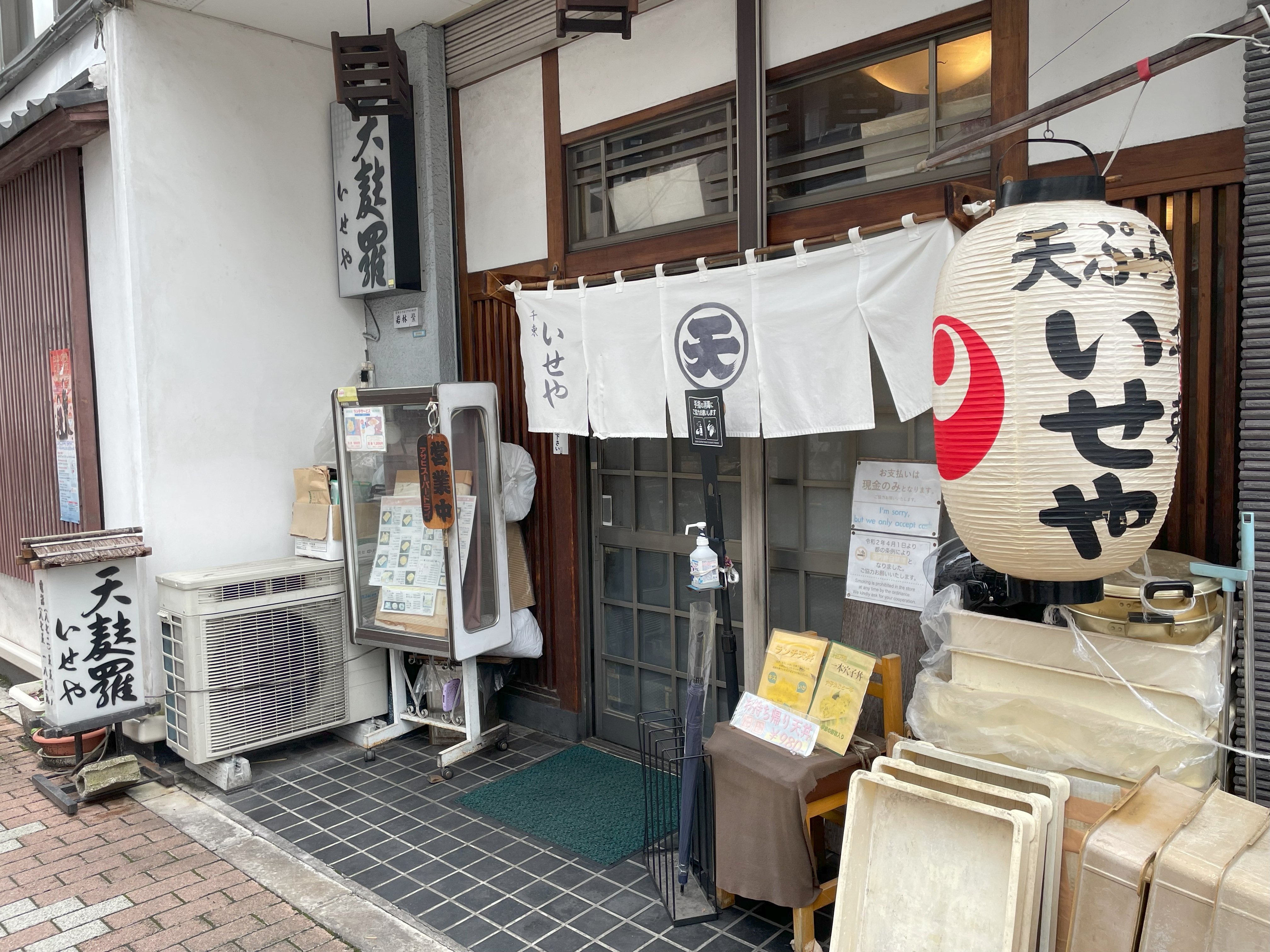 金美館通り沿いに佇むいせや千束さんの外観。ガラス張りのビル1階に白い暖簾が掛かる。