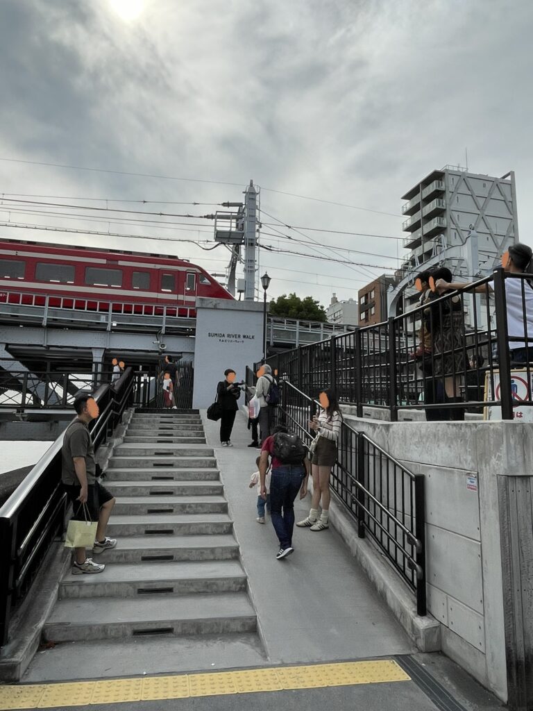 東武鉄橋の近くから、東武伊勢崎線の電車が浅草駅へ向かう様子を見る人々。