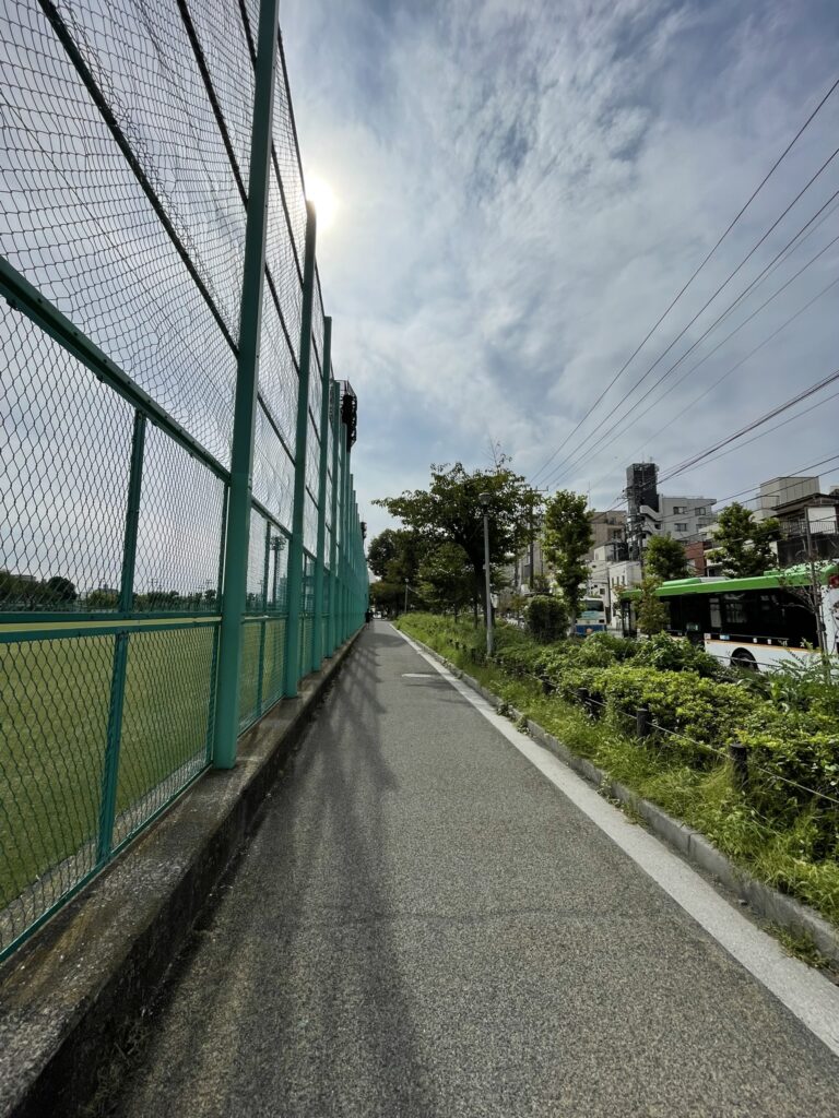 野球場を囲むフェンス沿いの道を歩く人。