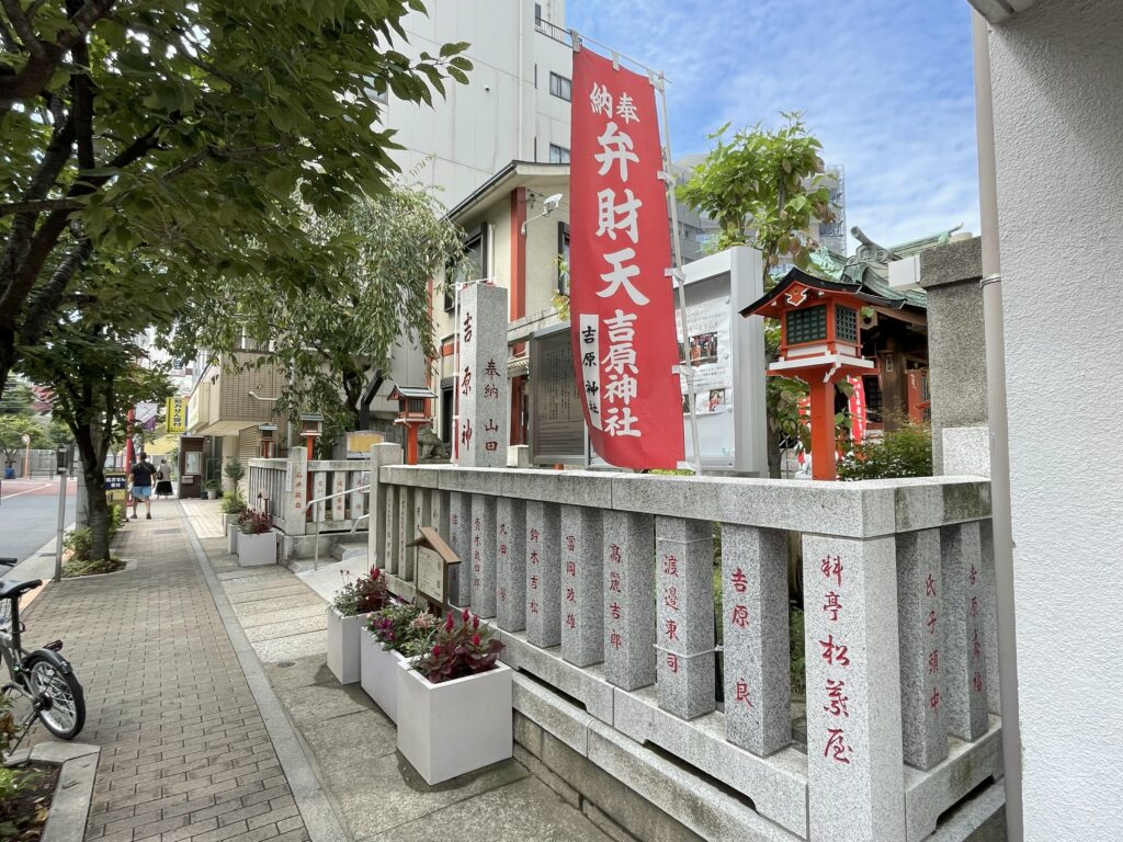 吉原神社の社号標と赤い幟旗が並ぶ仲之町通り。
