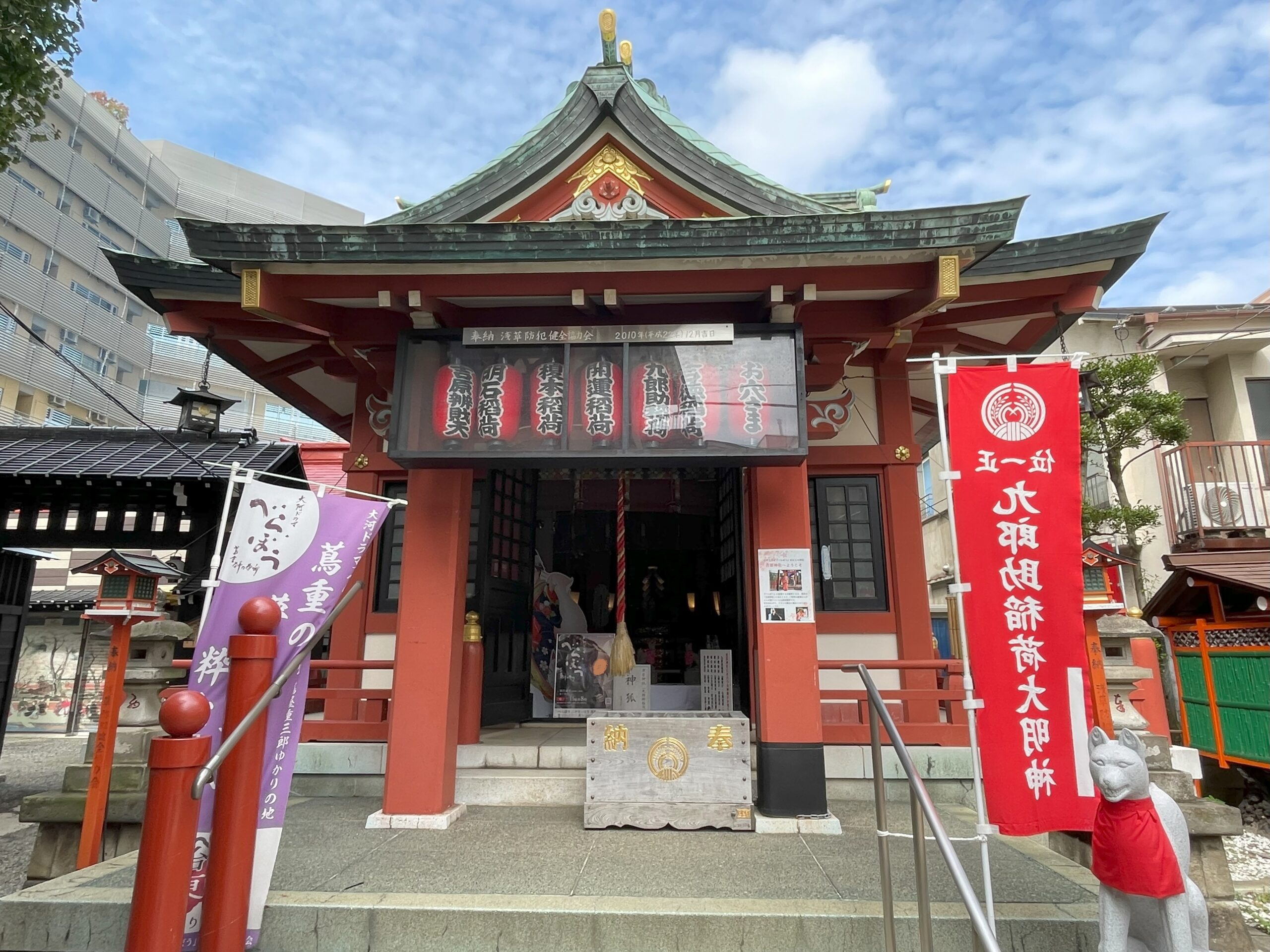 吉原神社の拝殿正面と赤い幟、「九郎助稲荷様」の神狐様の像。