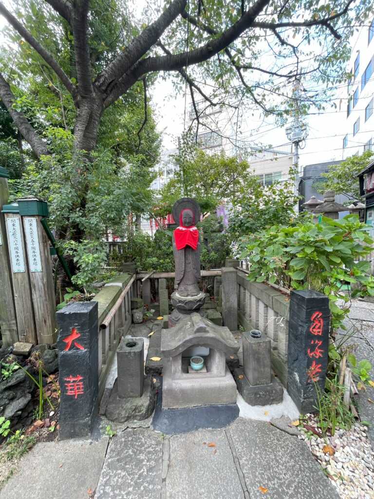 赤い前掛けを着けたお地蔵様と「大華」「角海老」と刻まれた黒石柱。