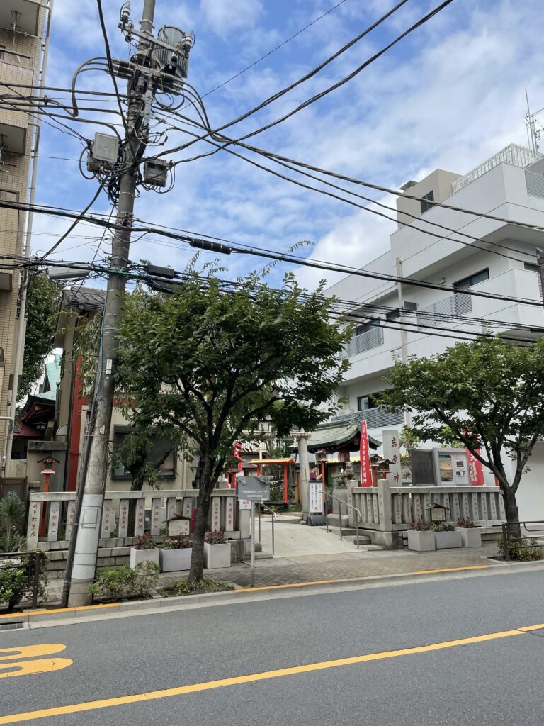 道路越しに見た吉原神社の全景と石鳥居、赤い幟が並ぶ境内の入口。
