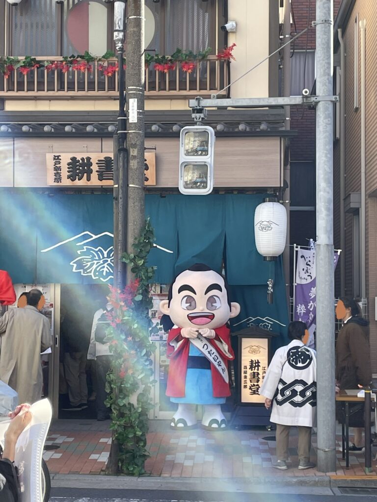 「江戸新吉原耕書堂」の店頭に、東京都台東区のマスコットキャラクター「つたいやん」が立っている。