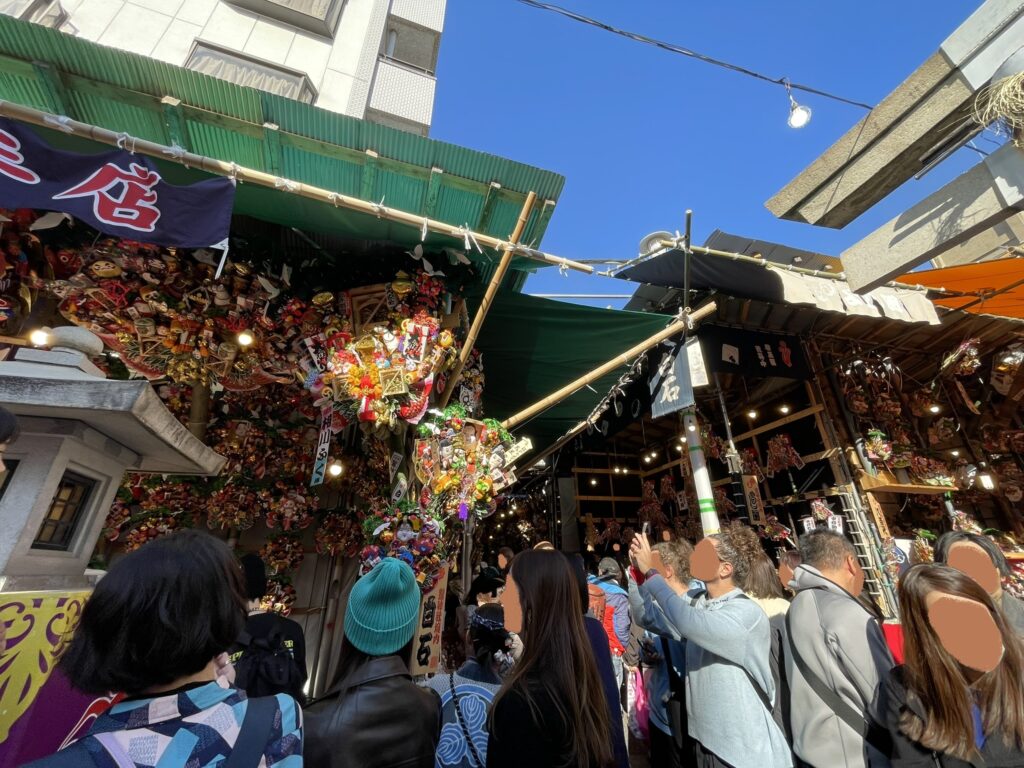 鷲神社の境内に立つ、たくさんの「熊手」の屋台。参拝者も写真を撮っている。