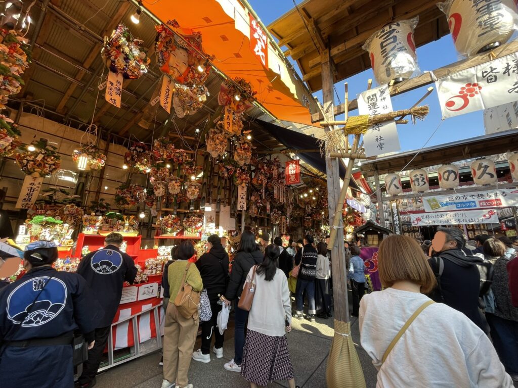 境内に飾られている「熊手」を参拝者たちが眺めている。