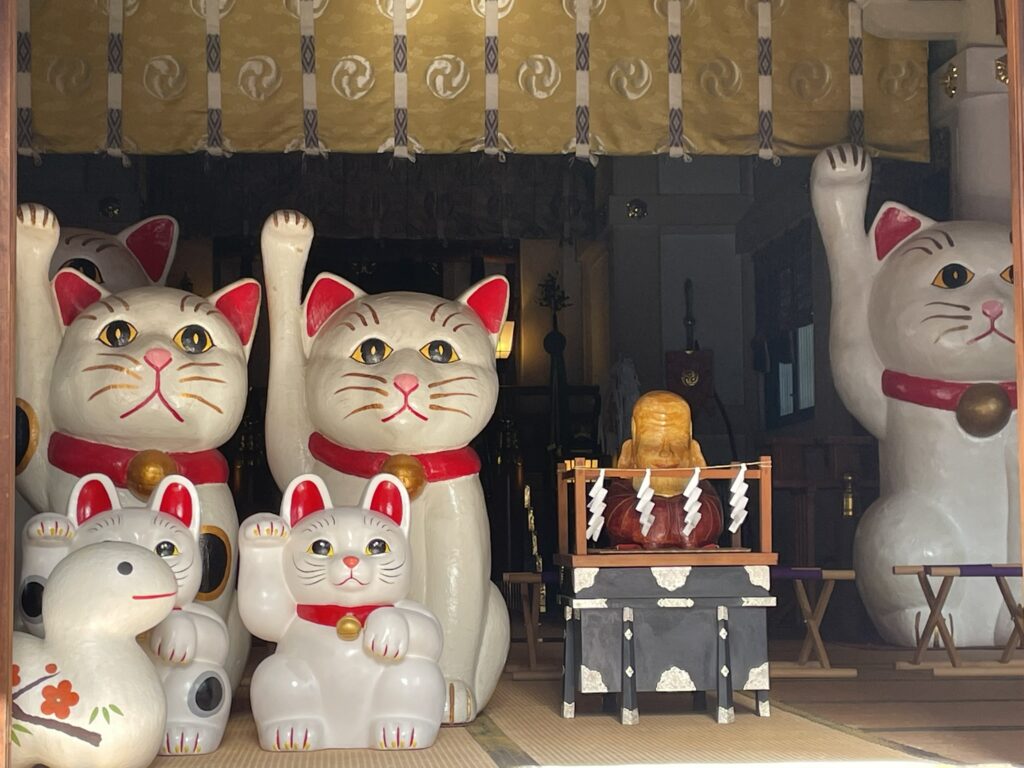 今戸神社の拝殿内。中央には祭壇が設けられ、参拝される方々を見守る、七福神の福禄寿（ふくろくじゅ）や干支の蛇、縁結びの象徴とされる招き猫たち。