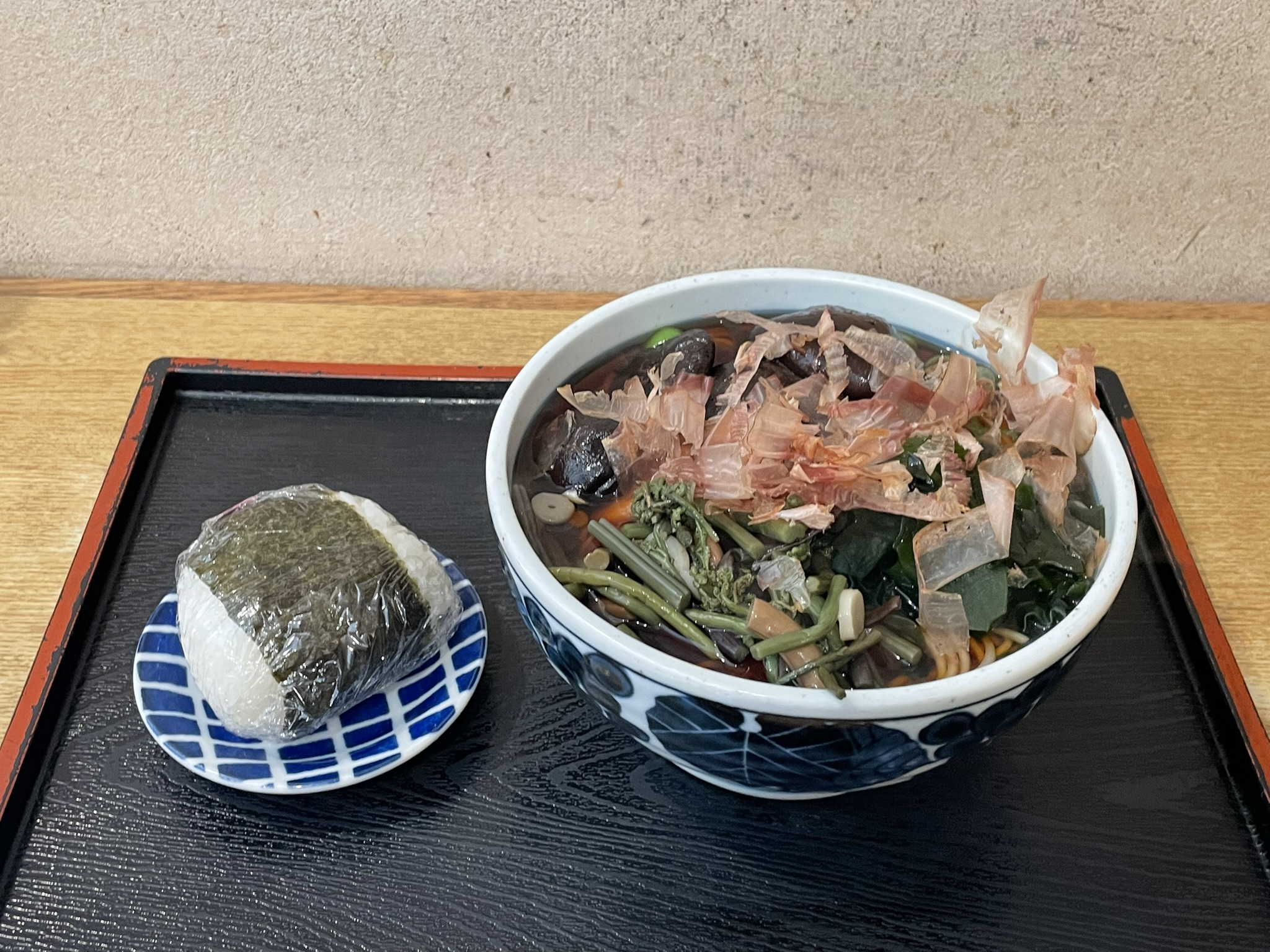 「めん処おばた」さんの「山菜そば」に「しいたけ」のトッピング、そして「おにぎりB」の写真。そばには、山菜、ワカメ、ねぎ、かまぼこ、花かつお、しいたけが添えられている。おにぎりは明太子。