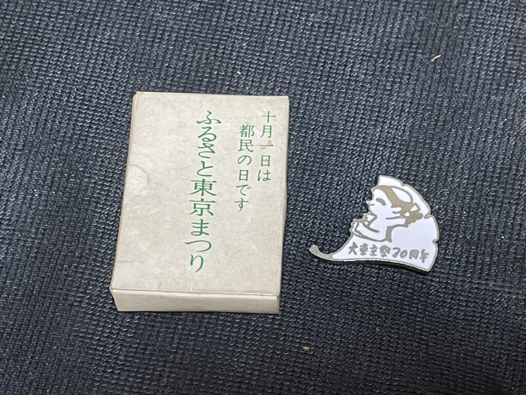 「カッパバッジ」と、バッジが入っていた「ふるさと東京まつり」「十月一日は都民の日です」と印字された白い紙箱。