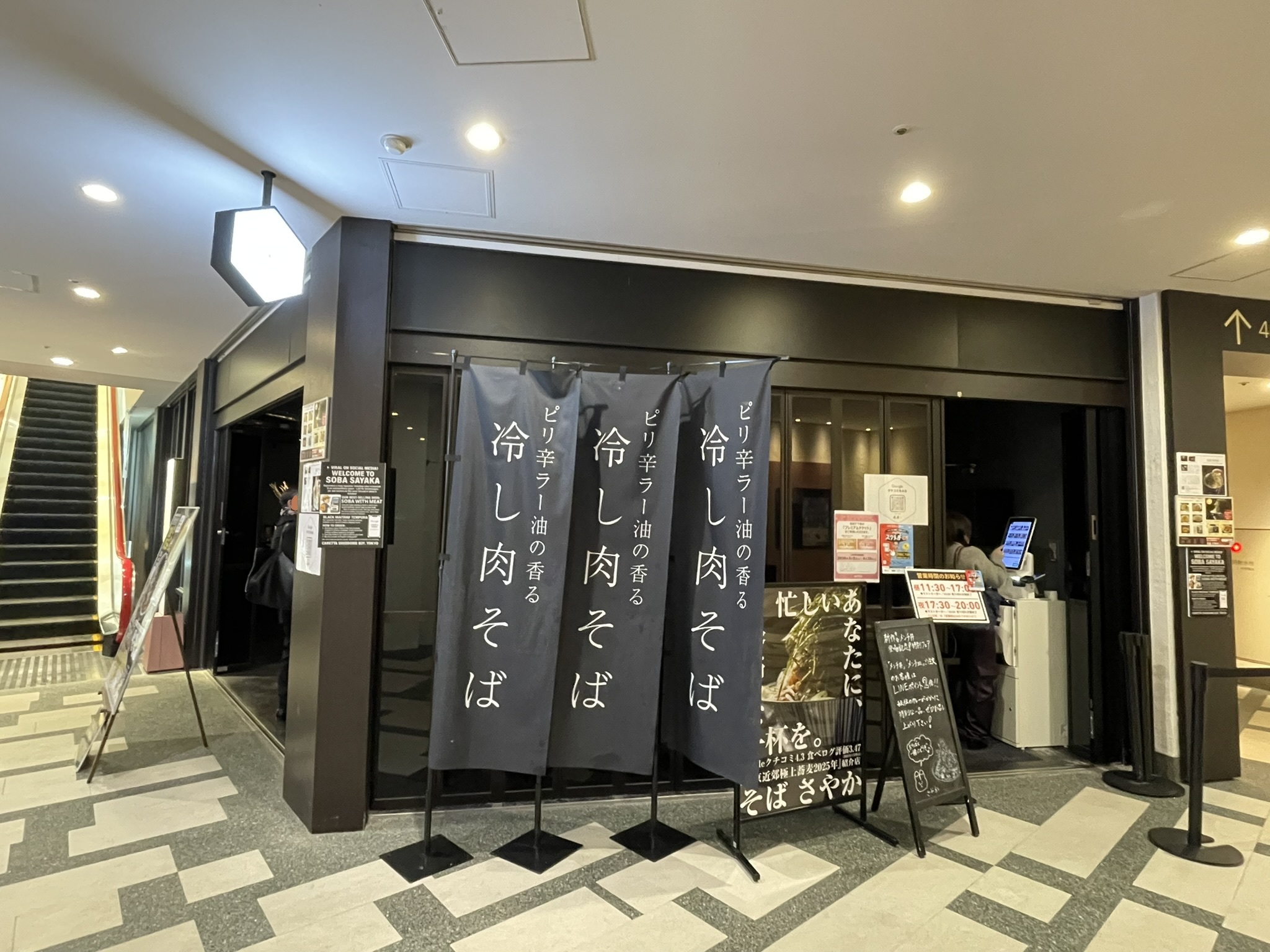 「そば さやか」さんの店舗外観。店頭には「ピリ辛ラー油の香る冷し肉そば」の黒いのぼりが並ぶ。