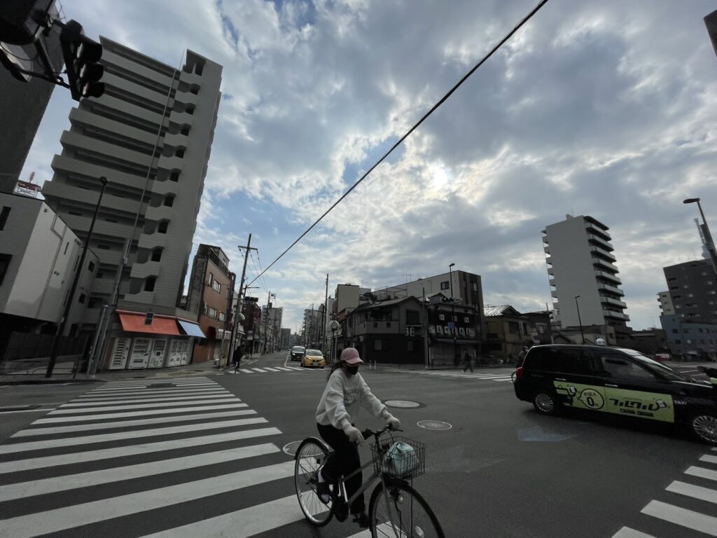 清川二丁目交差点を横断する自転車とタクシー。日常の動きがある山谷の街。