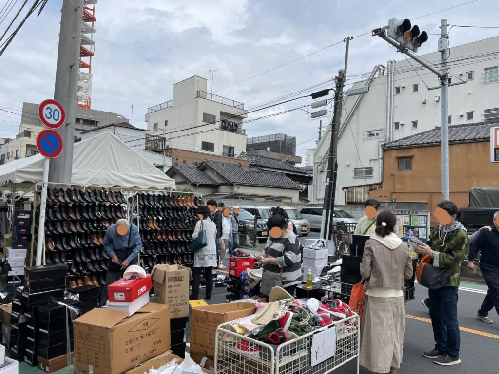 革靴がずらっと陳列された壁面ディスプレイが壮観な出店ブース。段ボール箱に積まれた在庫と、熱心に品定めをする来場者の姿。