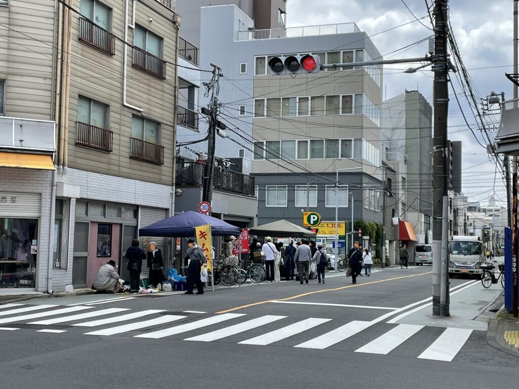 交差点の一角に「キムチ」の黄色い幟とテントが見える。玉姫稲荷神社周辺の路地にも露店が広がり、お祭りの賑わいが街中にあふれ出している。
