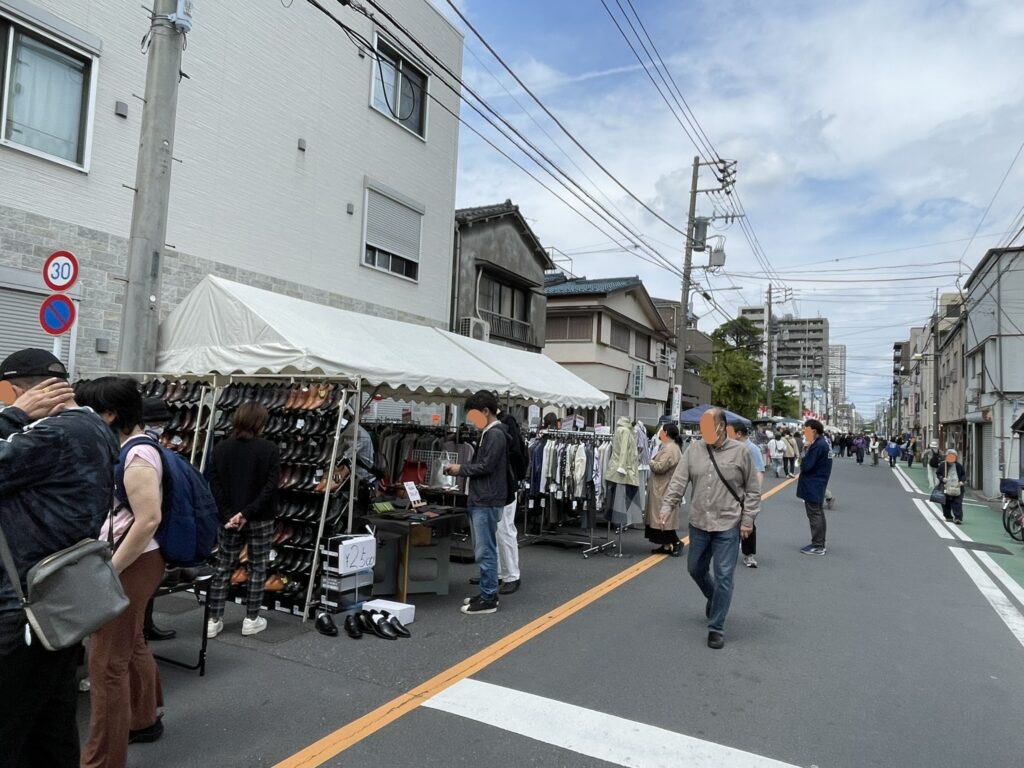 革靴やブーツが並ぶテント前で、来場者が熱心に品を選ぶ。奥には衣料品の出店も続き、靴市の会場が通り沿いに長く伸びている様子がわかる。