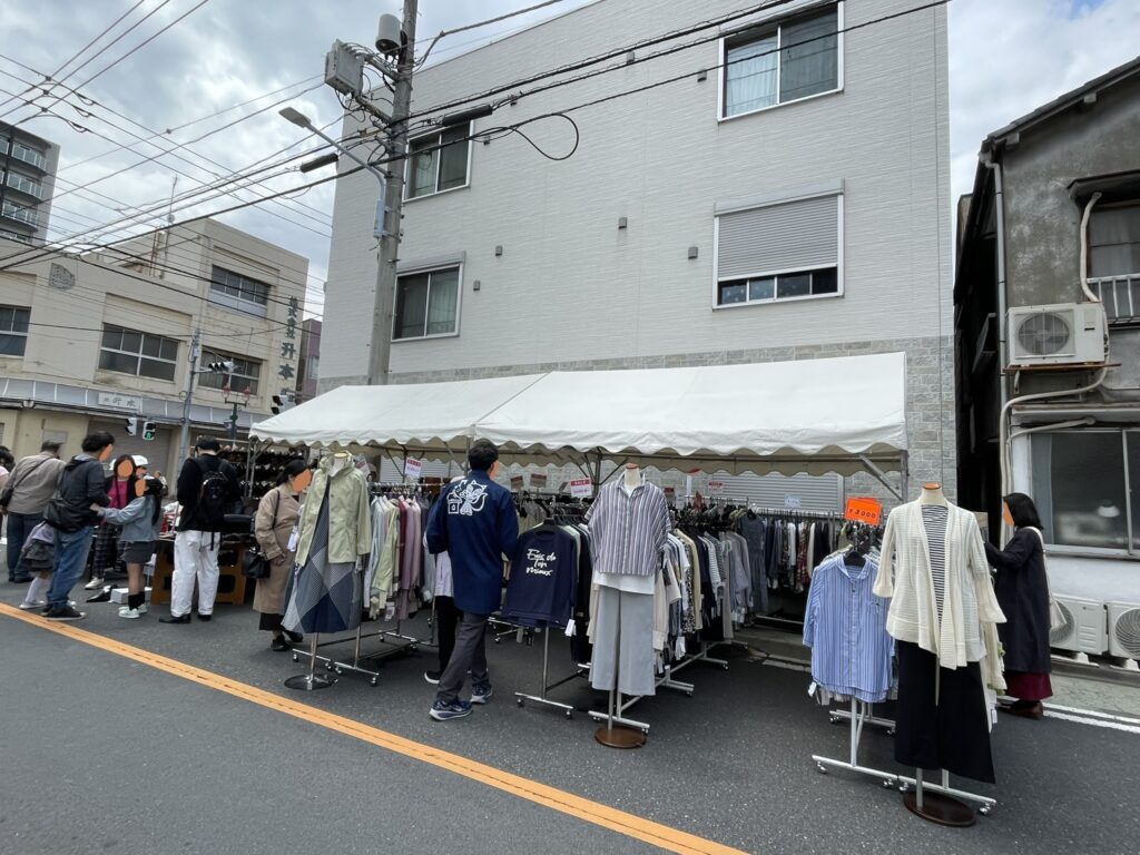 ハンガーラックに春物の衣料品が並ぶ出店コーナー。靴だけでなく、バッグや衣類なども取り揃えられており、「靴の祭り市」の幅広いラインナップを物語る。