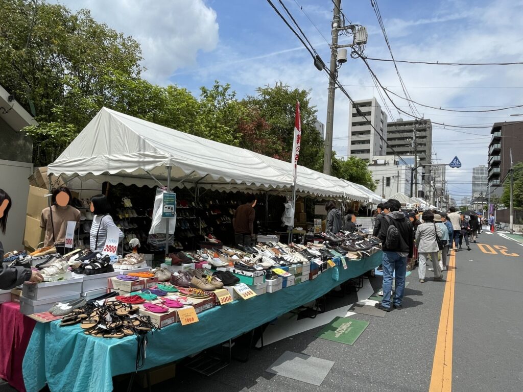 テント下に靴がずらりと並ぶ販売コーナー。1,000円〜3,500円の値札が並び、サンダルやスニーカーなど多彩な靴が来場者を迎える。