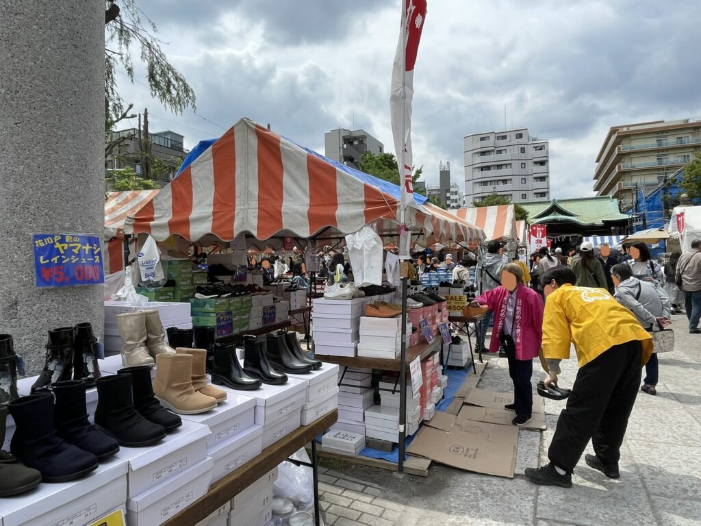 境内の参道沿いに並ぶブーツや雨靴のコーナー。「ヤマナシ レインシューズ ¥5,000」の手書きPOPが添えられ、黄色い法被を纏った出店者が来場者に対応している。