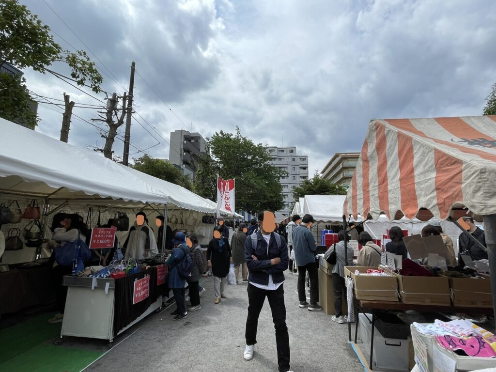 「こんこん靴市」の幟を背に、イタリア製牛革バッグや雑貨が並ぶ通路。靴だけでなく皮革製品全般が揃い、「靴の祭り市」が革製品の総合市場であることがわかる。