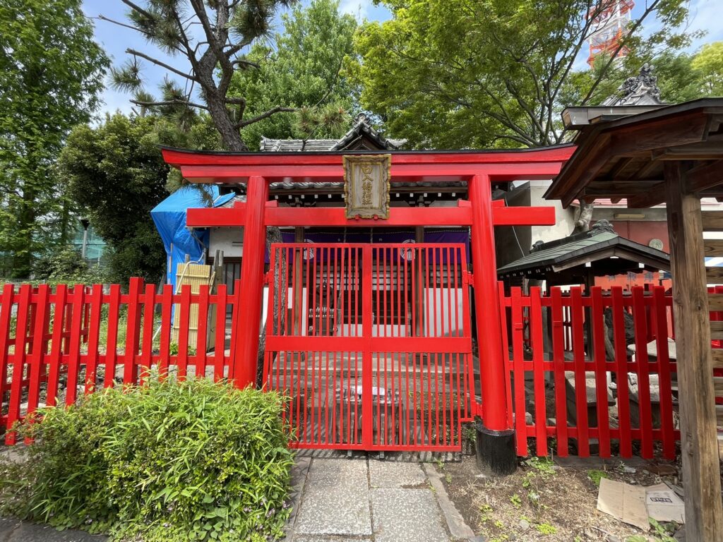 境内に鎮座する「口入稲荷社」の朱色の鳥居と赤い柵。緑豊かな木々に囲まれ、祭りの喧騒の中にひっそりと佇むこの一角が、神社の歴史ある奥行きを感じさせる。