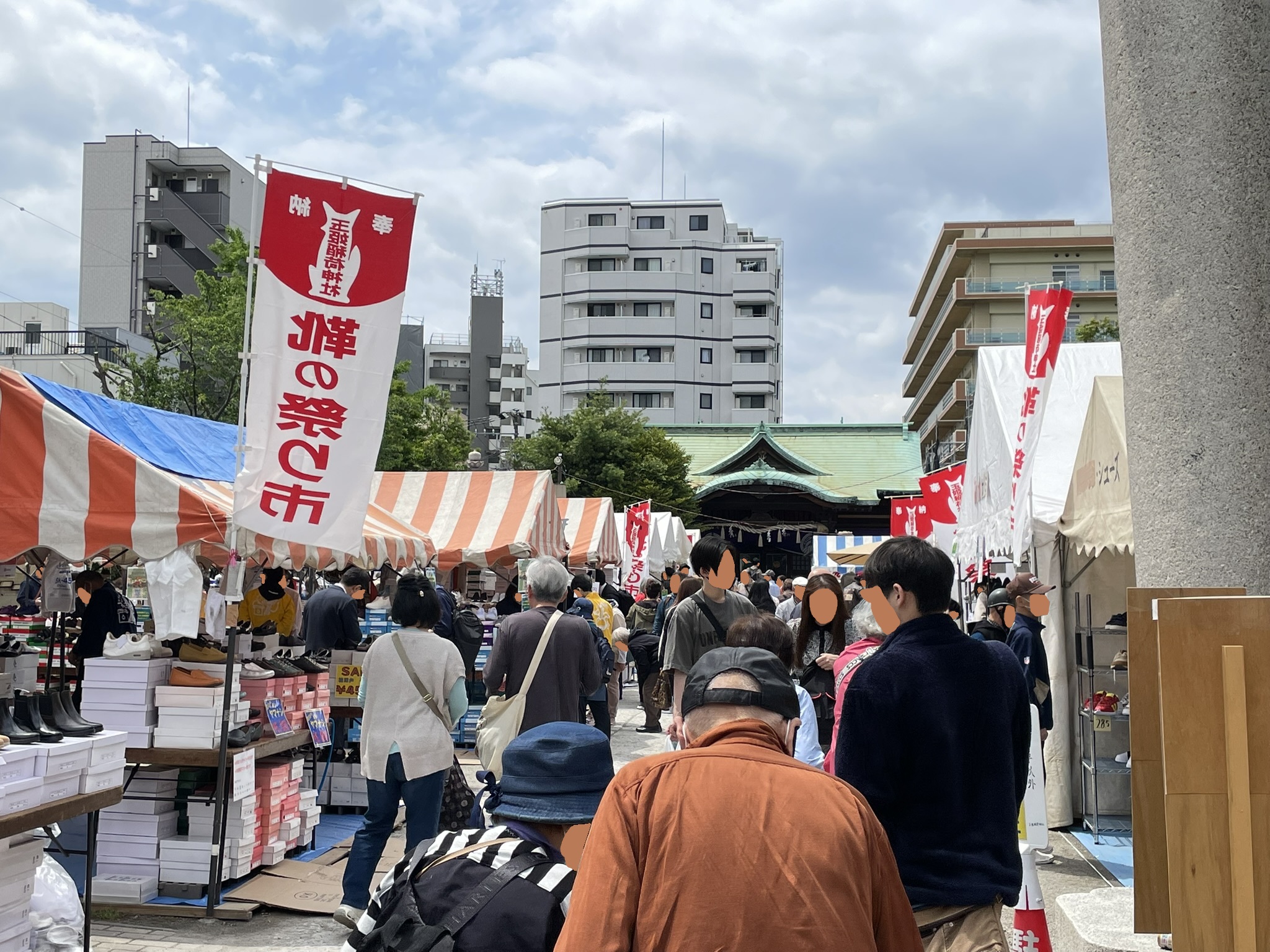 「靴の祭り市」の幟の向こうに、玉姫稲荷神社の社殿が望める。境内を埋め尽くす出店と人波の奥にお社が見えるこの構図が、1974年から続く「靴への感謝」という祭りの本質を静かに伝えている。