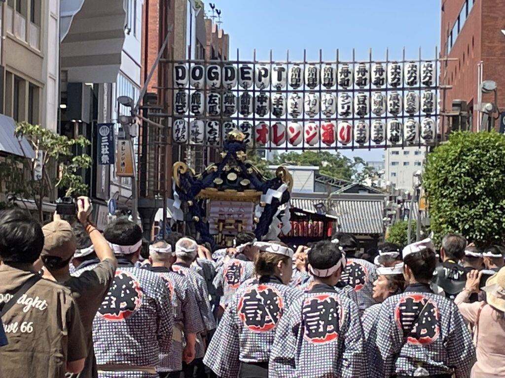 オレンジ通りを行く法被姿の担ぎ手たち。揃いの法被の背中が祭りの一体感を表しています。
