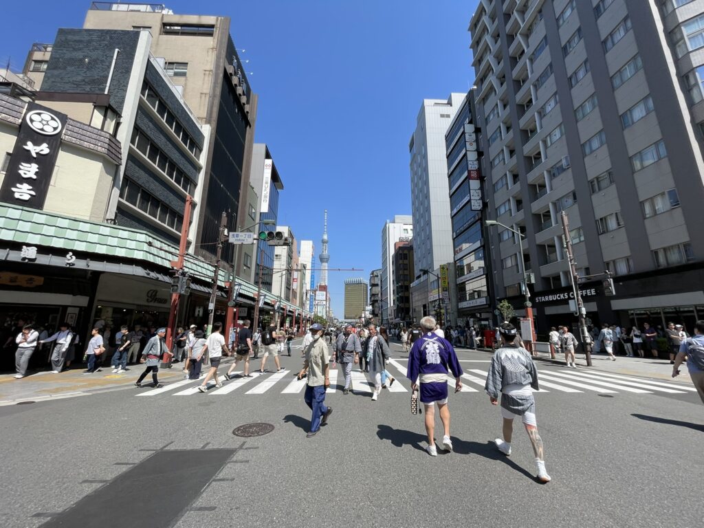 お神輿が巡行する雷門通り。青空の下、担ぎ手も観客も笑顔です。