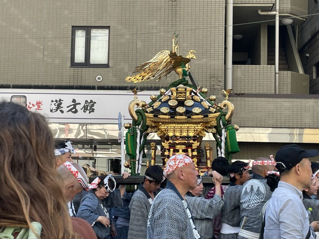 馬道通りを練り歩く神輿行列。金色の装飾が陽光を受けて輝いています。