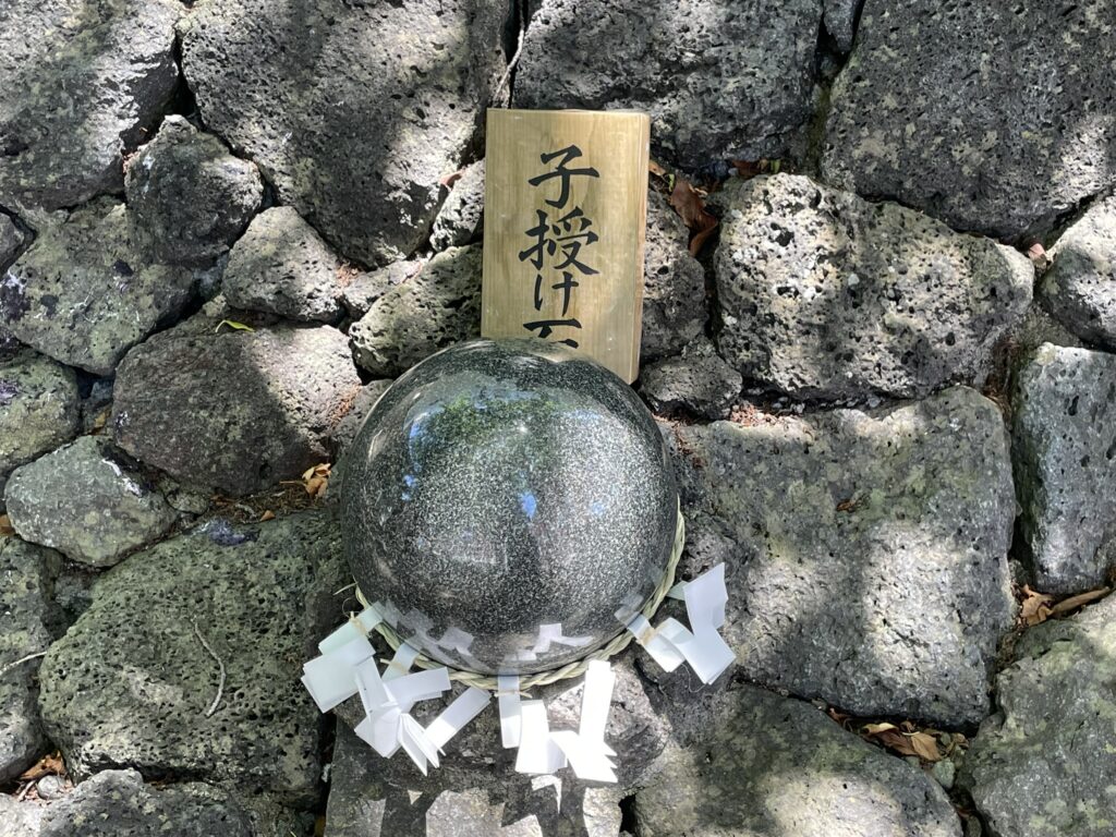 浅草富士浅間神社の富士塚にある子授け石。「子授け石」の木札とともに、しめ縄をまとった緑がかった丸石が置かれている。
